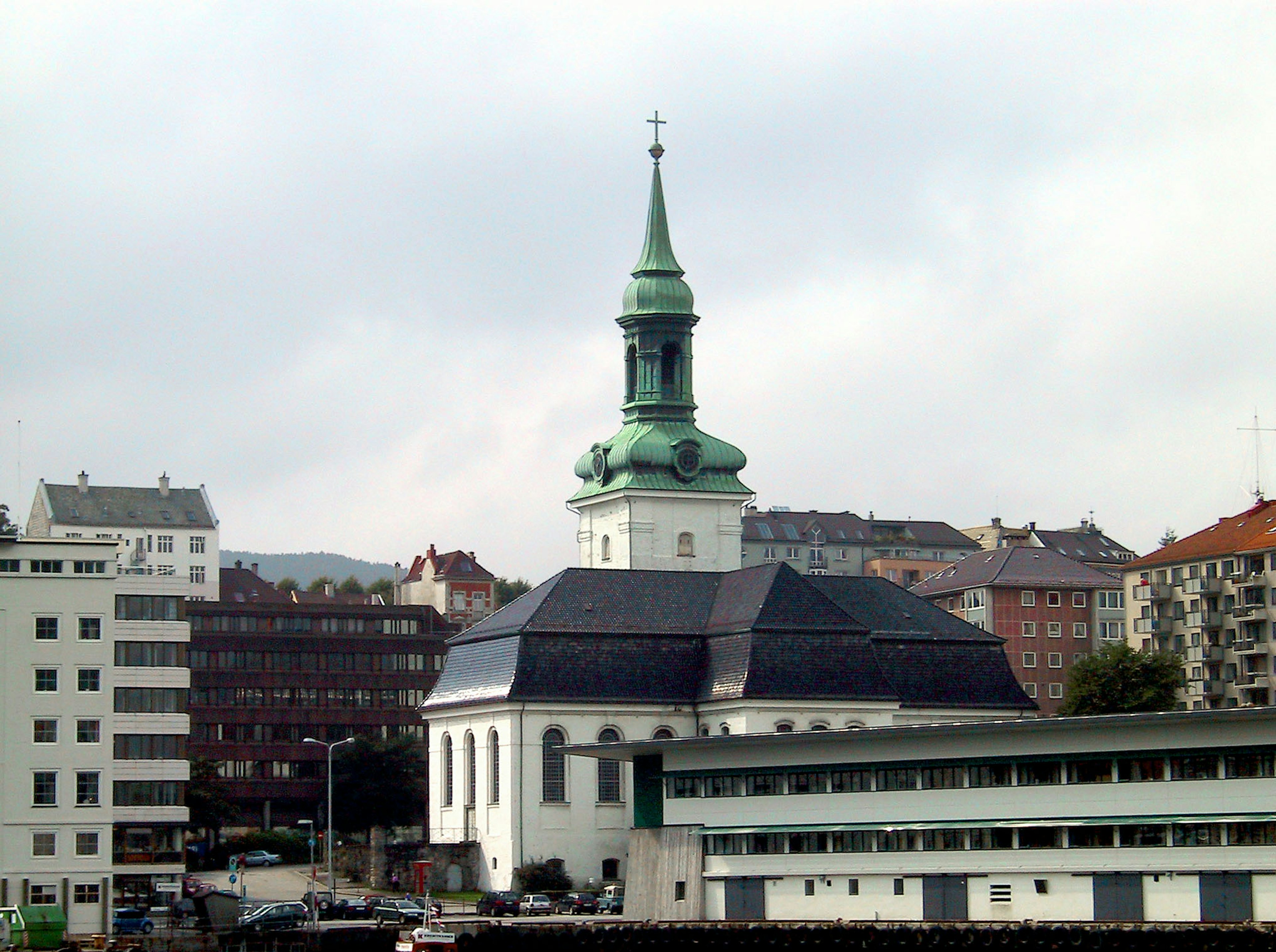 Vista di una chiesa con una guglia verde circondata da edifici moderni