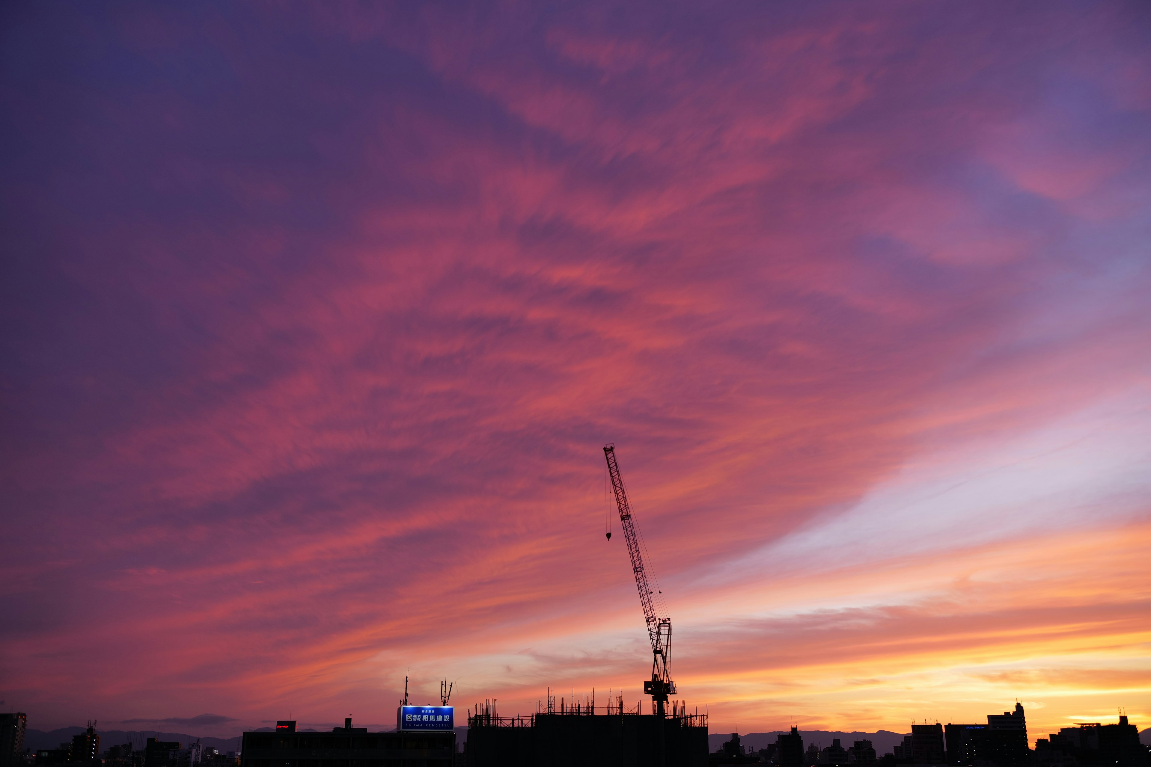 夕焼けの空に広がる紫とオレンジの雲と建設クレーン