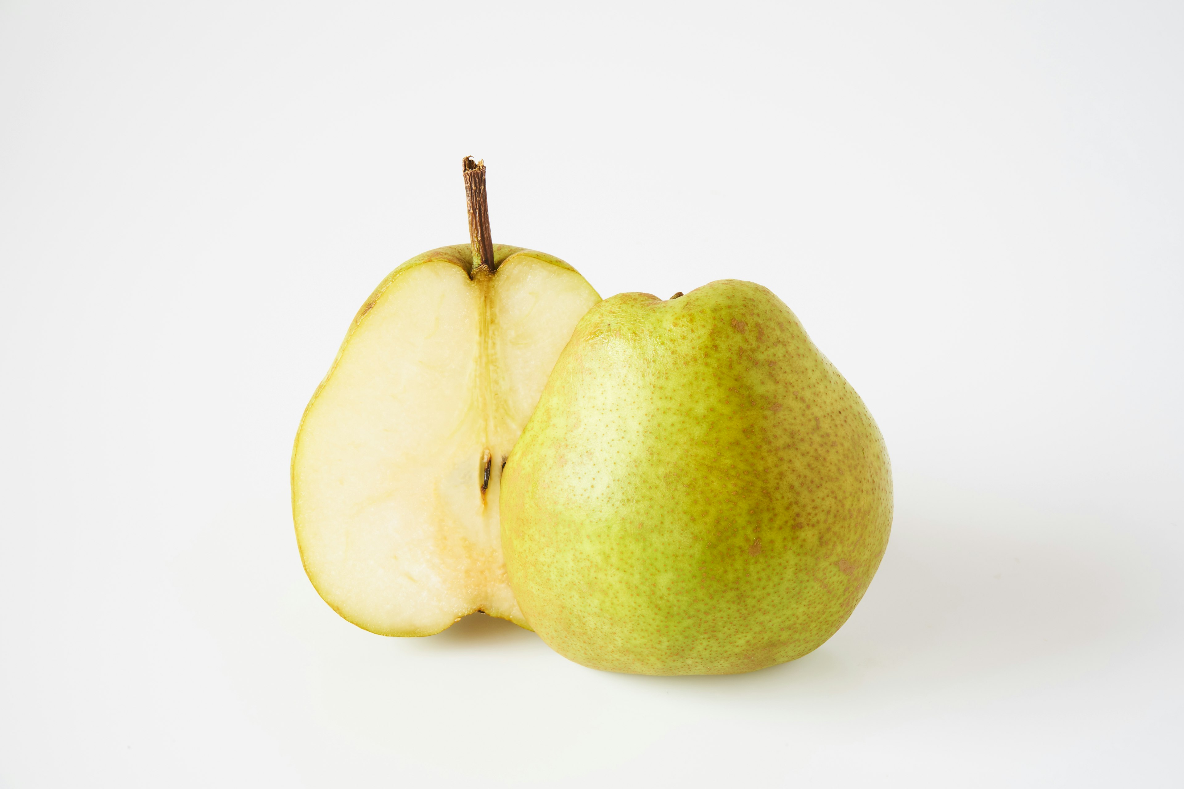 A whole green pear next to a sliced half on a white background