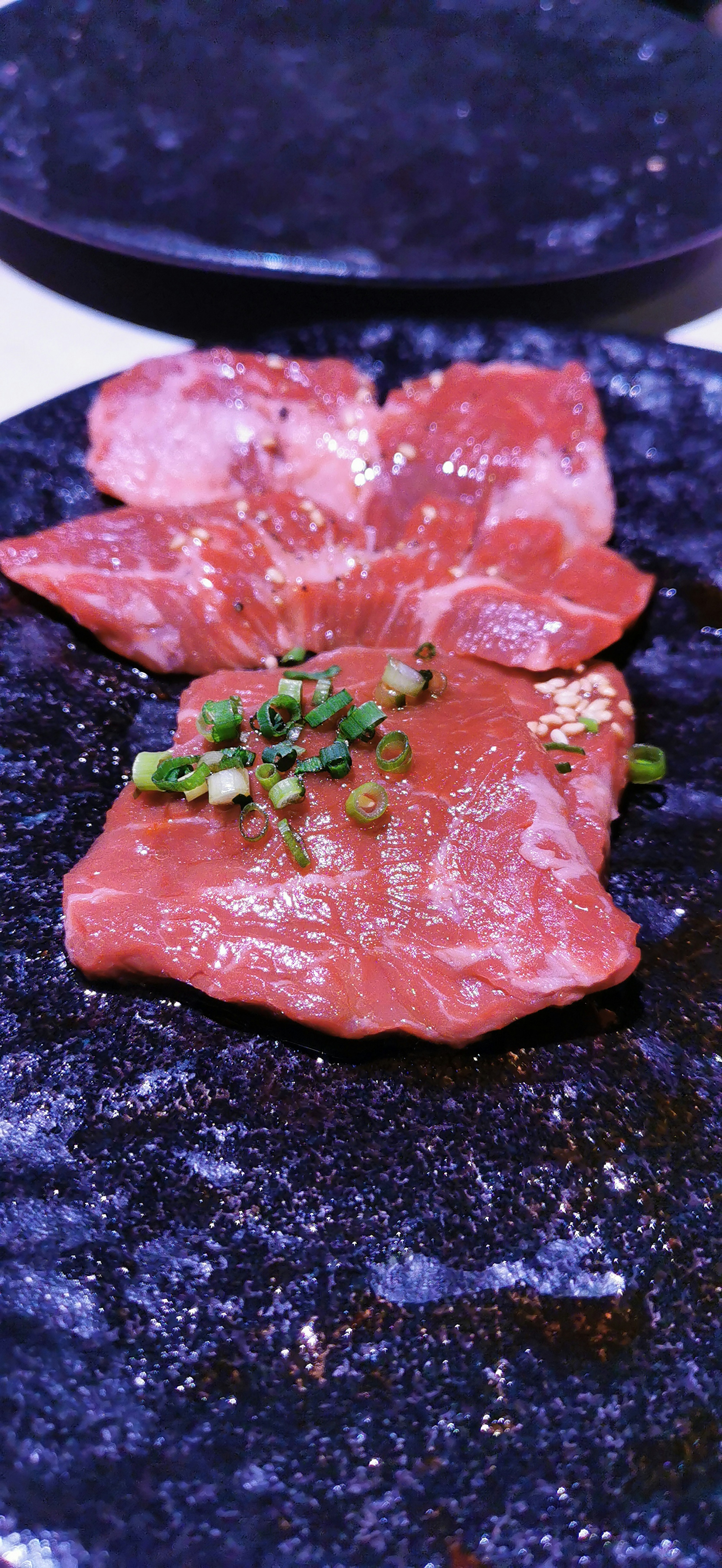 Viande tranchée sur une assiette noire garnie d'oignons verts