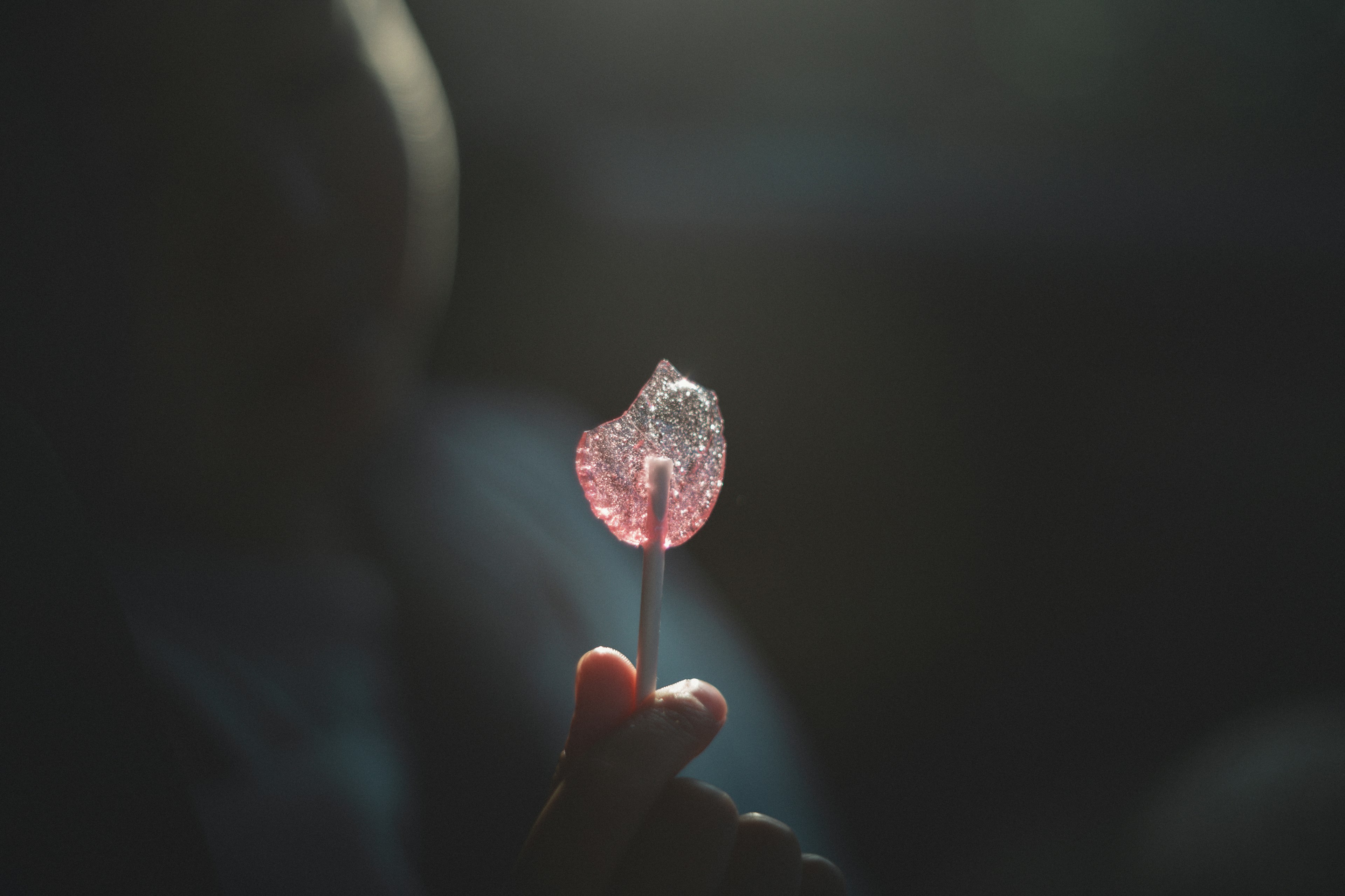 Lollipop merah muda dipegang di tangan dengan latar belakang gelap