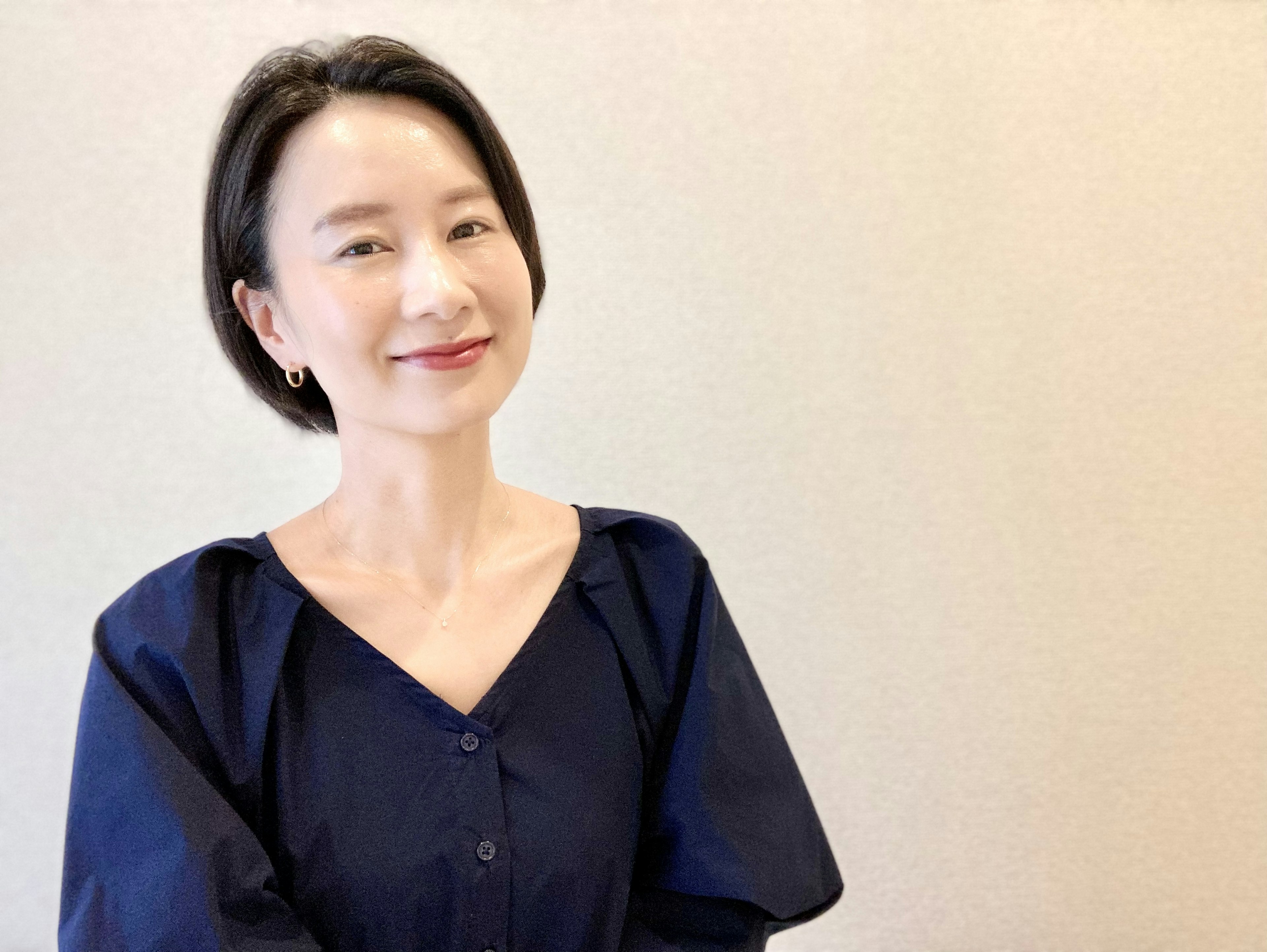 Smiling woman with short black hair wearing a navy blouse against a light background