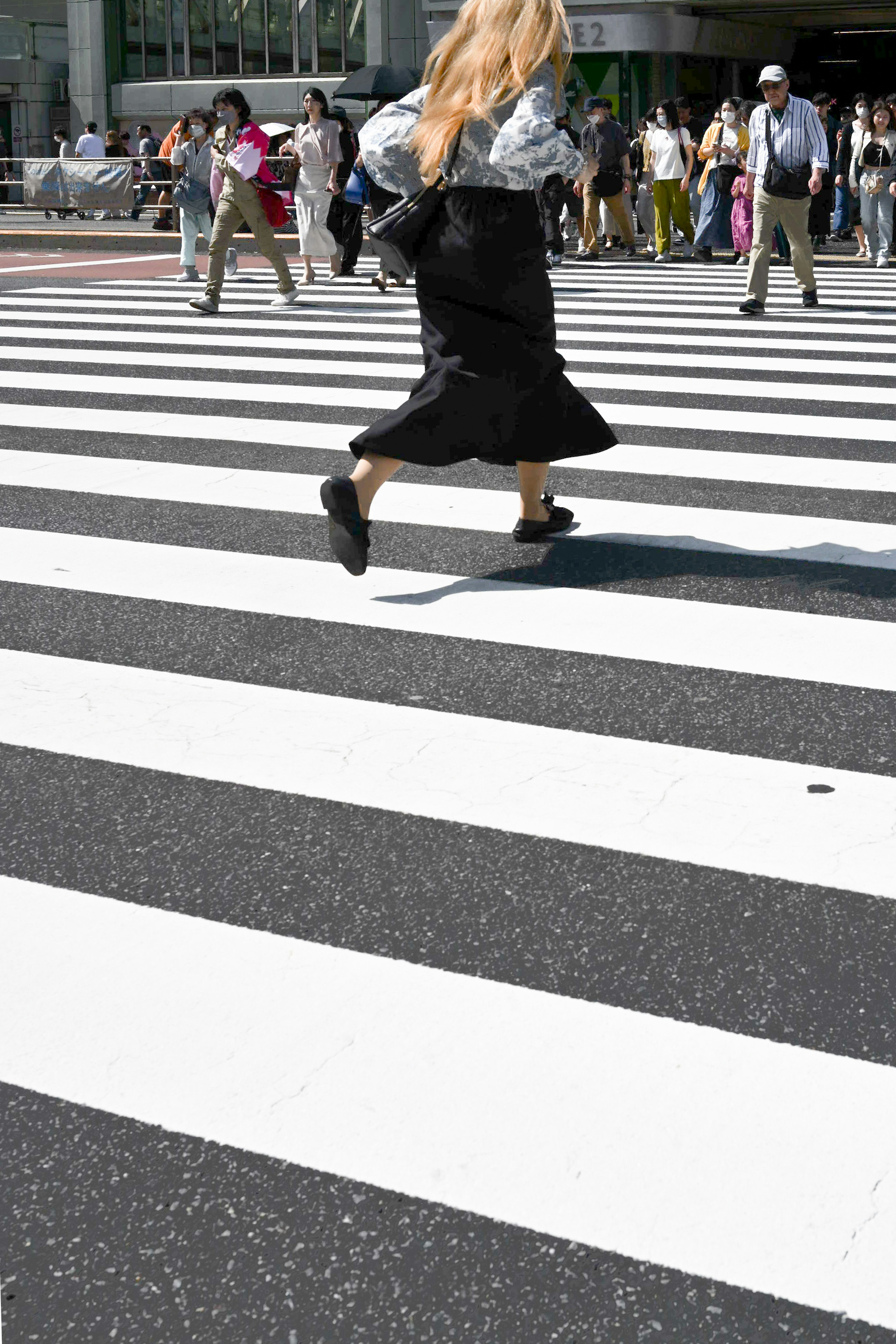 Mujer rubia cruzando un paso de peatones blanco y negro rodeada de gente