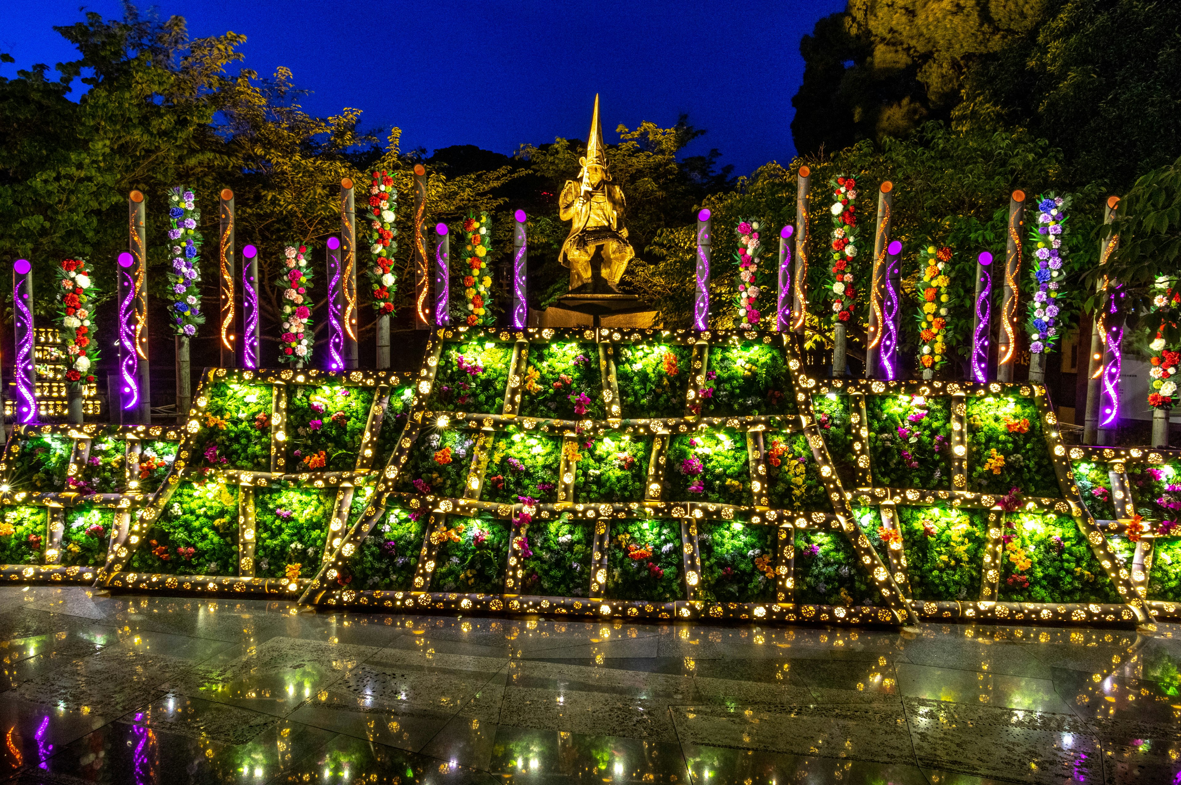 A beautifully illuminated garden with green decorations and a statue under the night sky