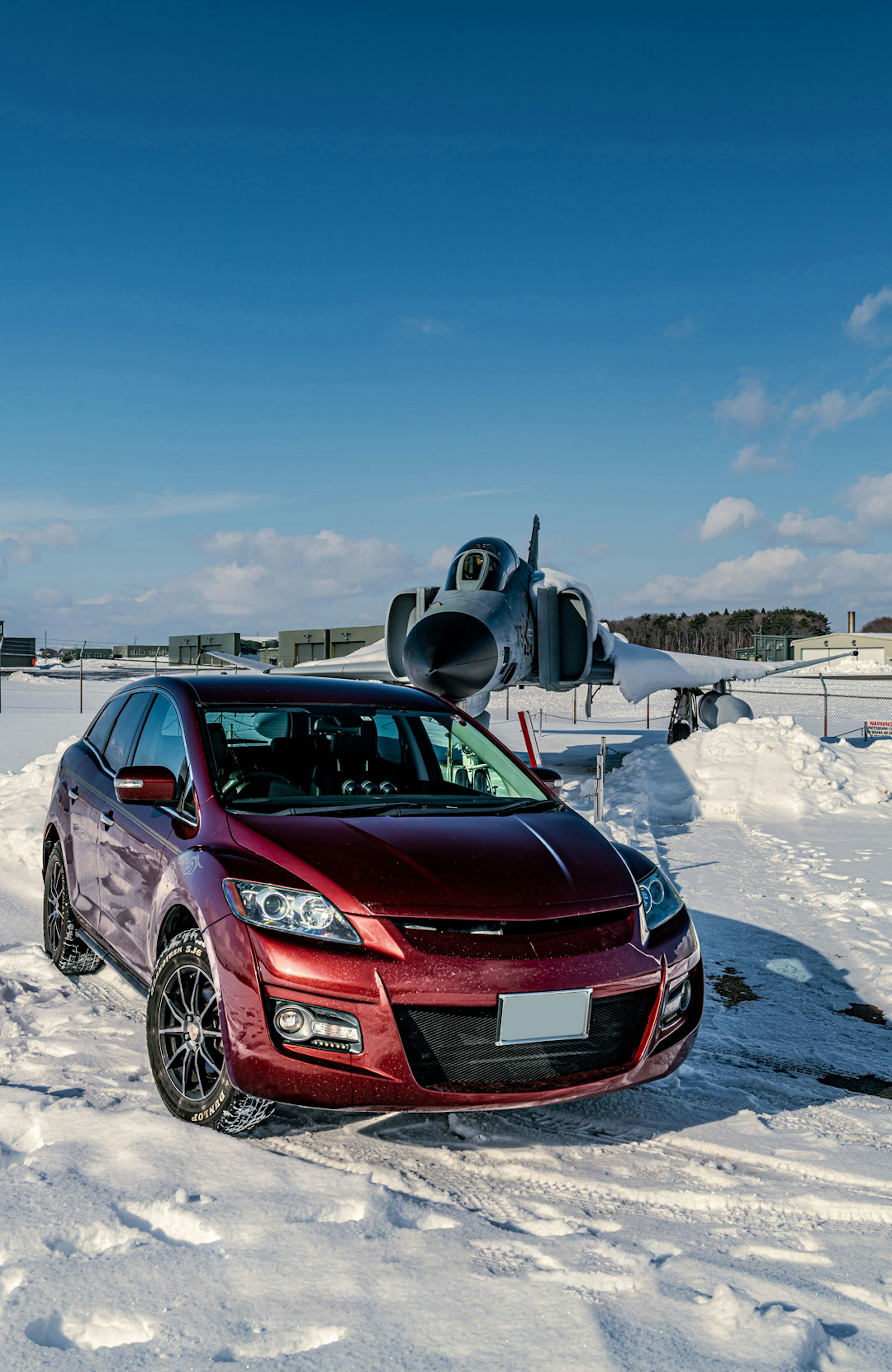 Red car parked in snow with an airplane in the background