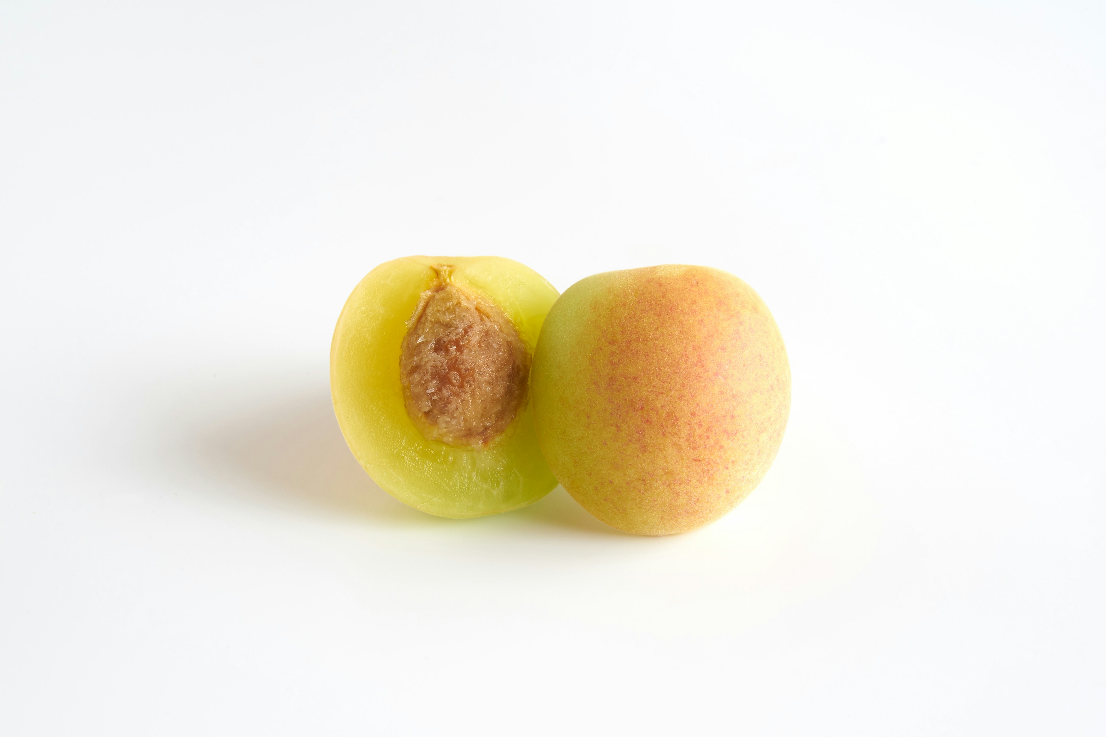 Two fruits touching each other with a greenish outer skin and a brown seed visible