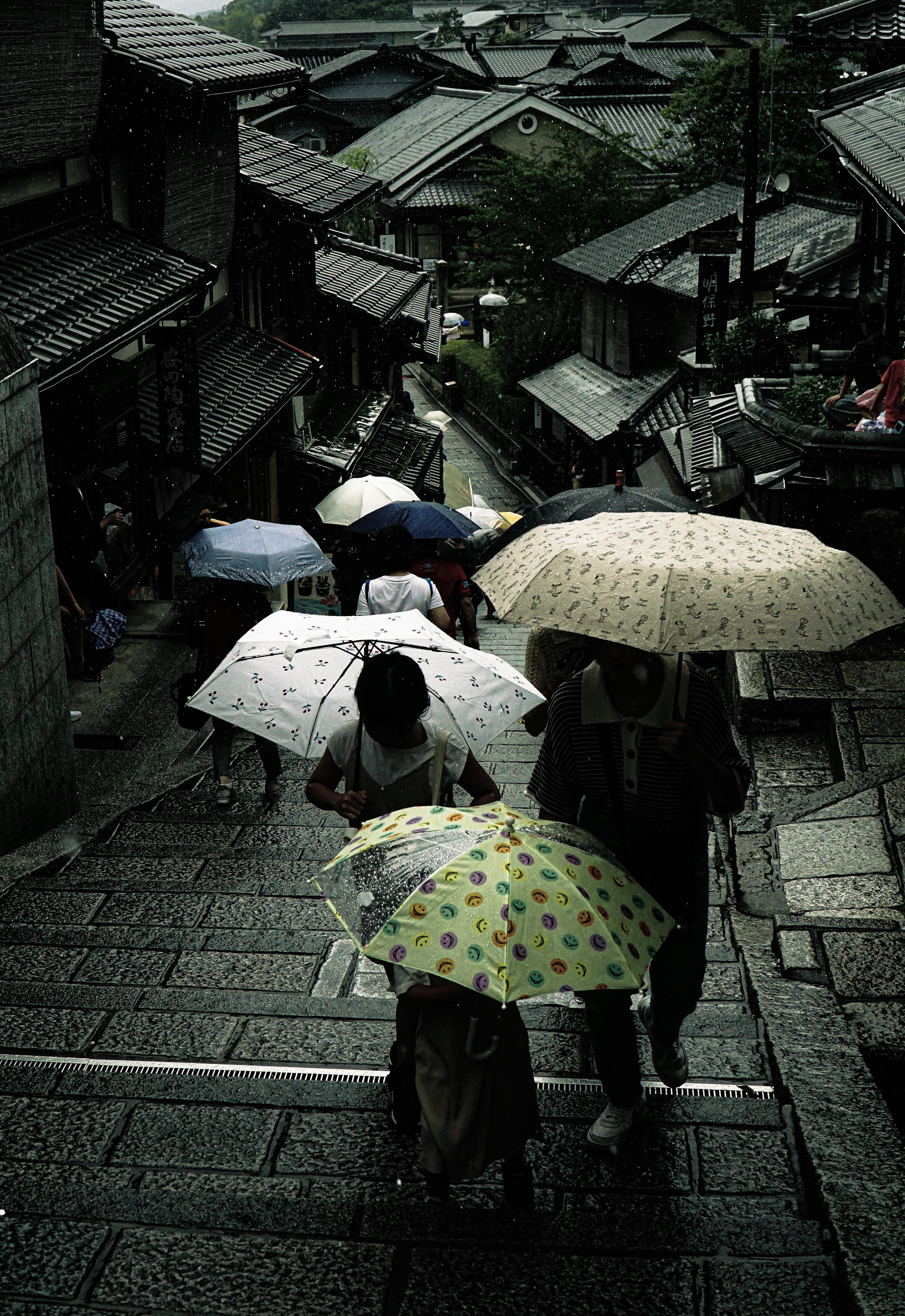 人々が傘をさして石段を下る風景 古い町並みが背景にある