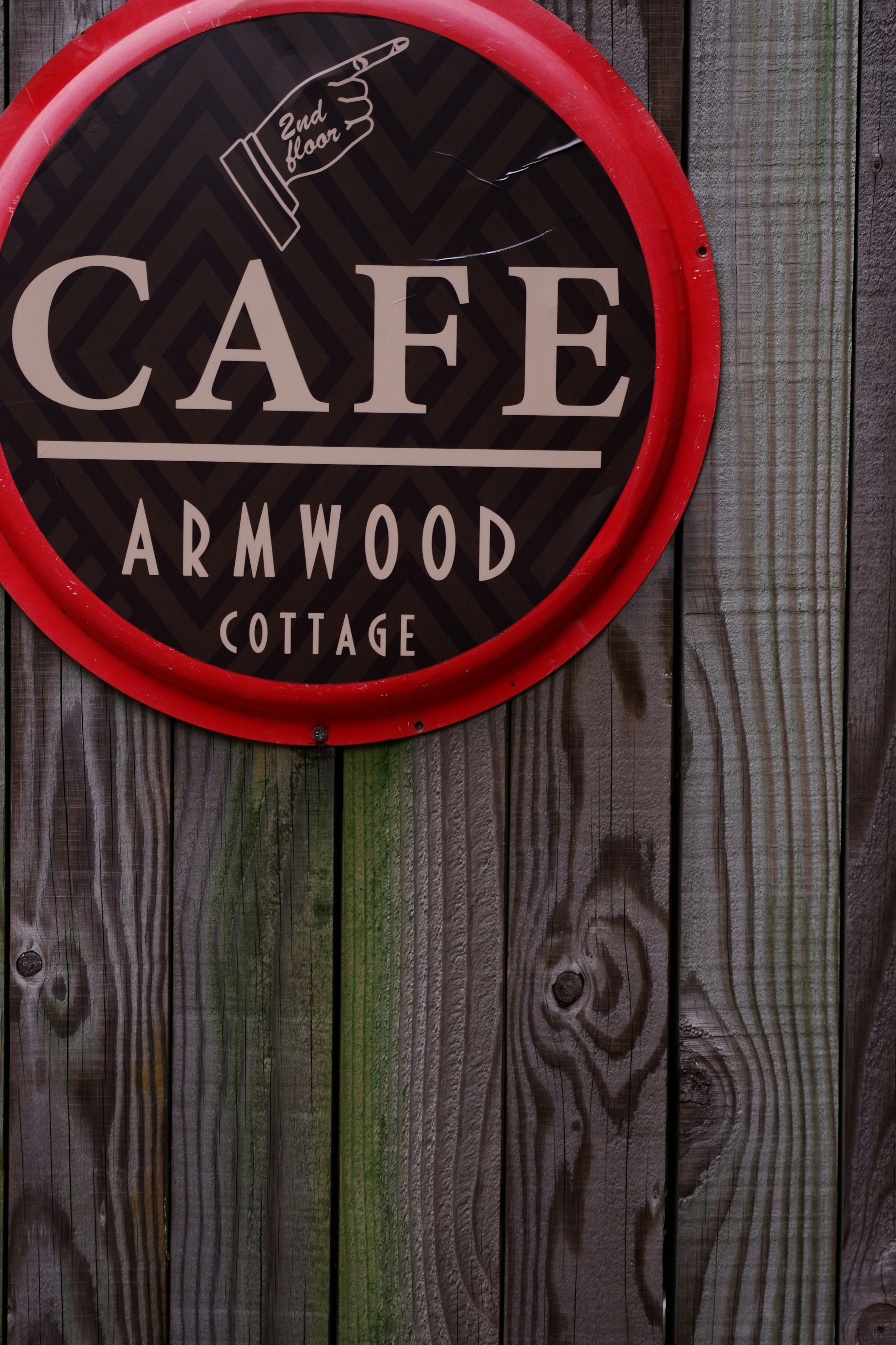 Round red sign displaying Cafe Armwood Cottage on a wooden wall