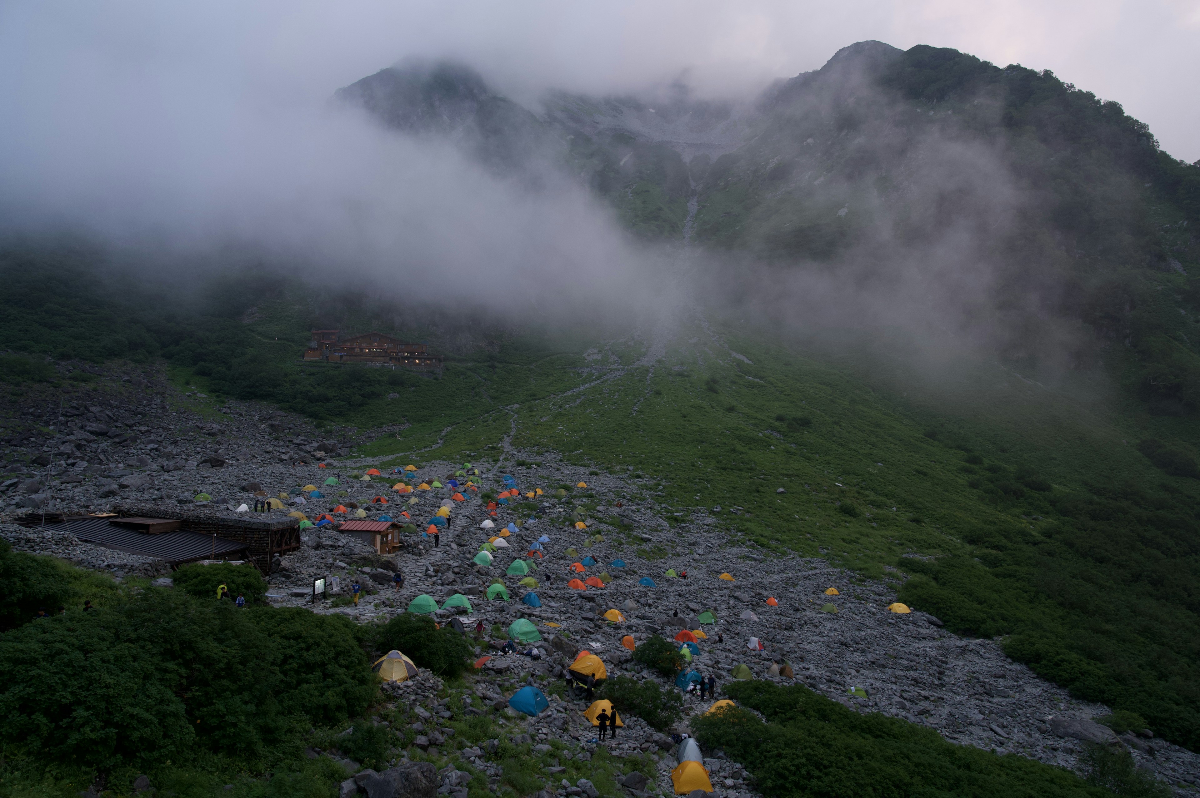 霧に包まれた山の斜面に設営されたカラフルなテント群