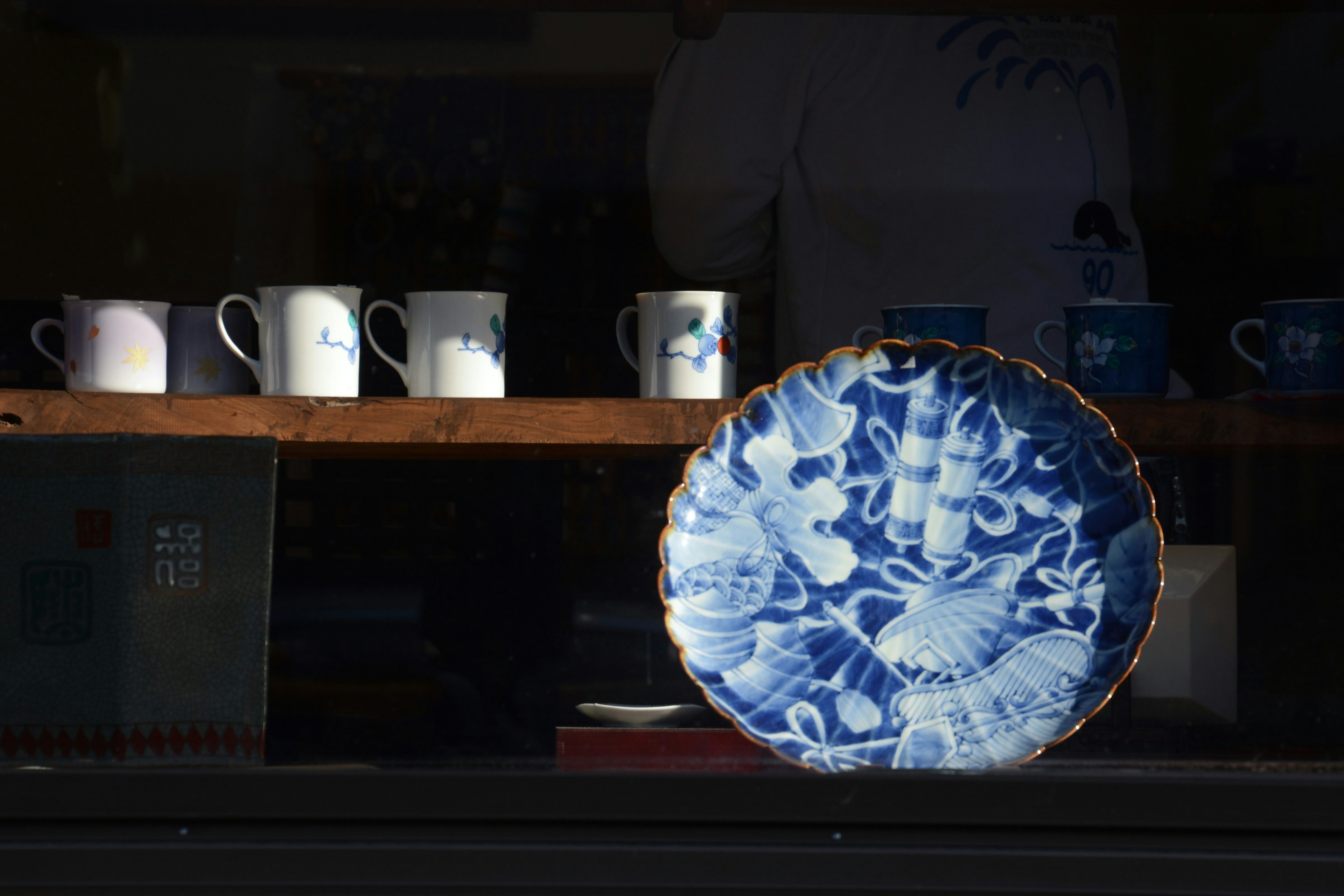 Un plato azul con flores y tazas blancas en una ventana de tienda