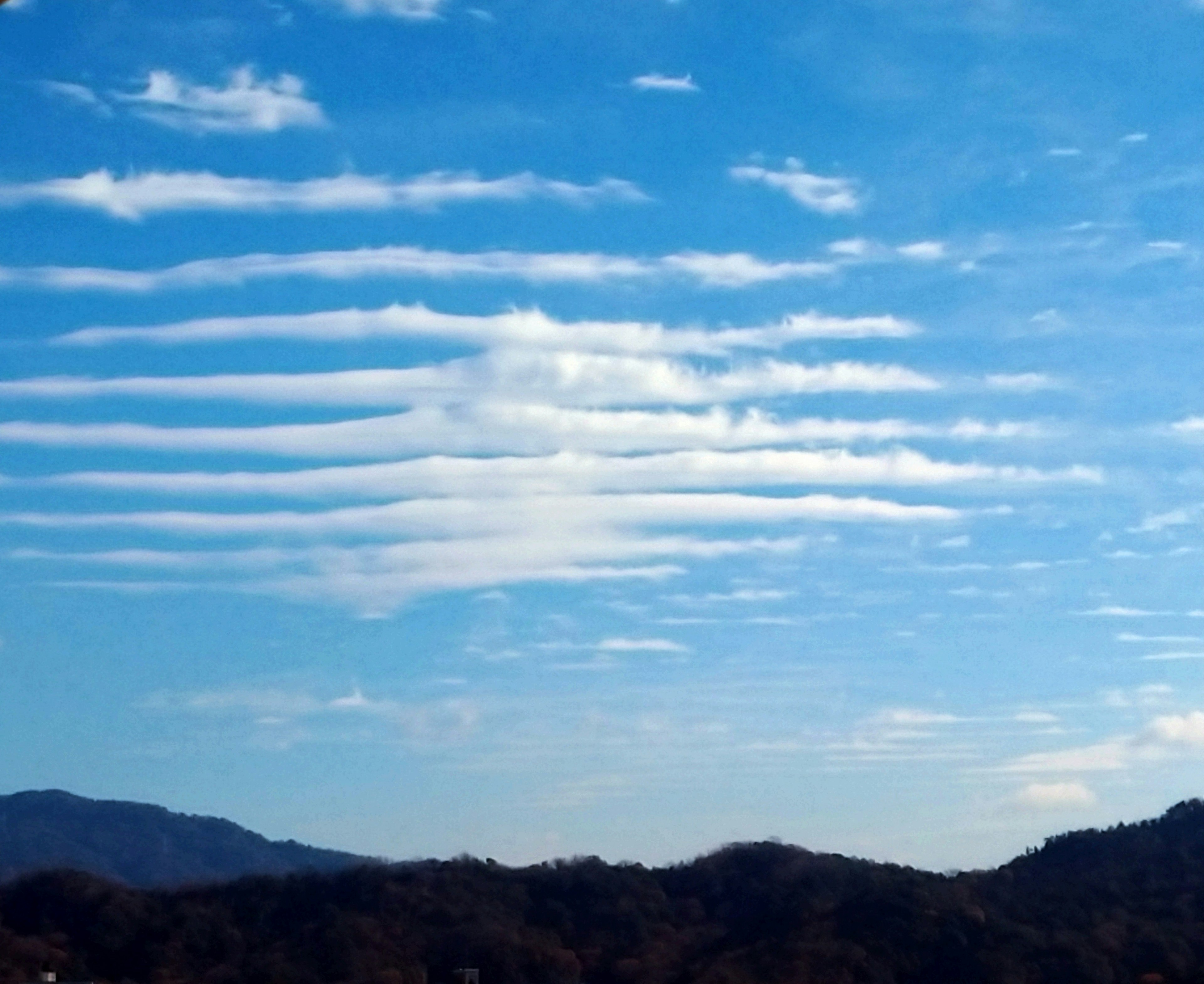 青空に浮かぶ波状の雲と山のシルエット