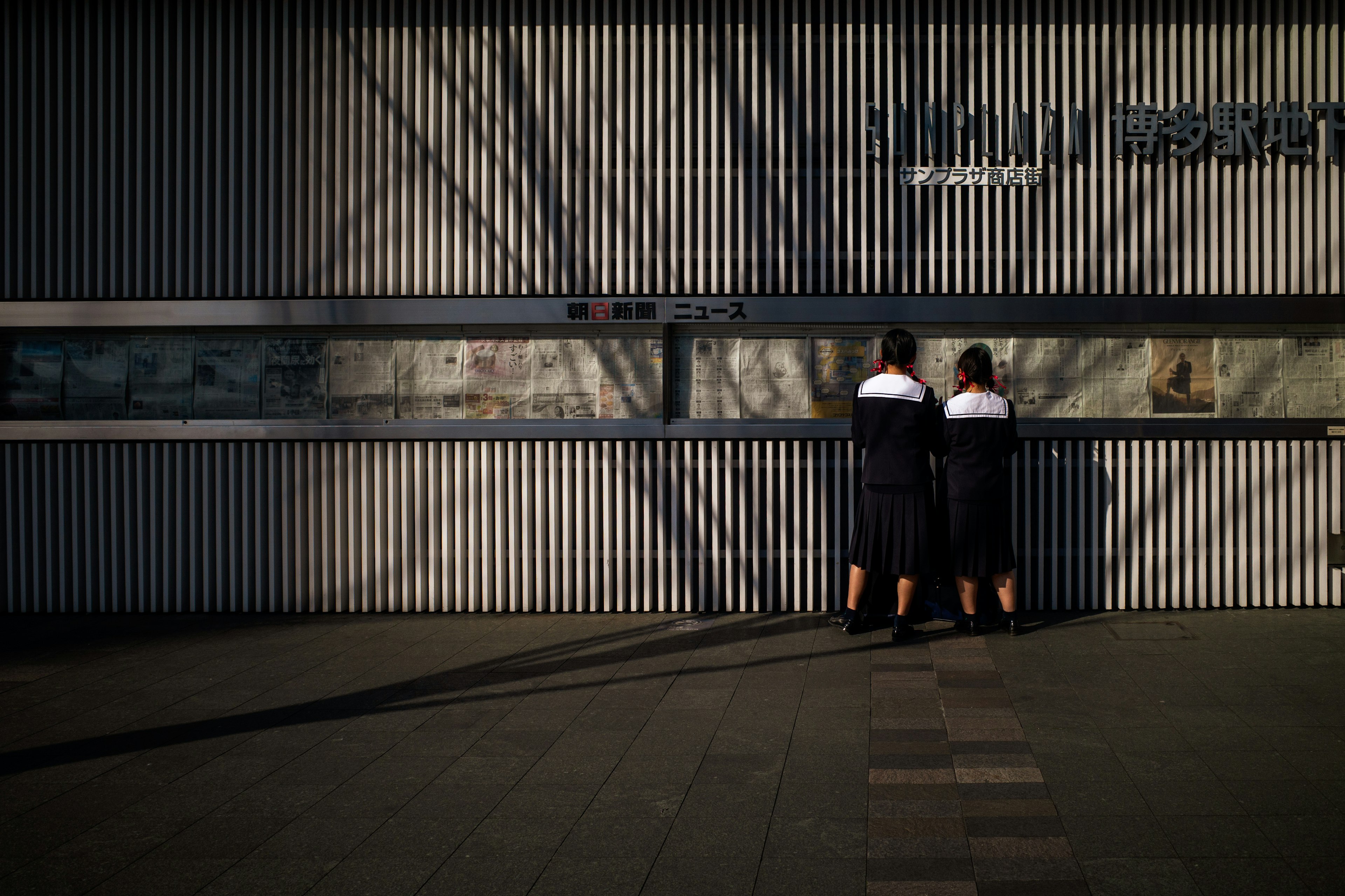 Two women standing in front of a vertical striped wall casting shadows