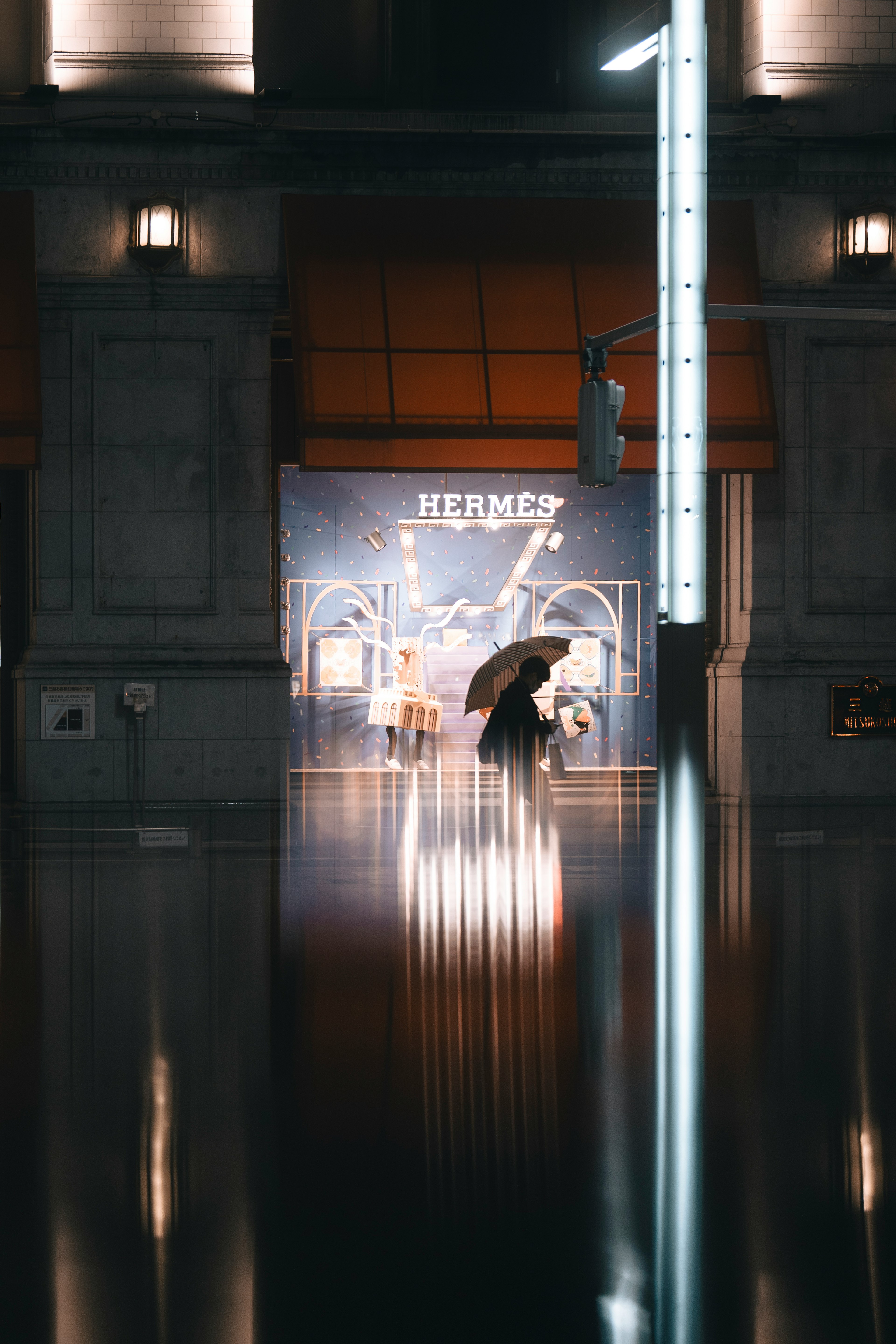 A person holding an umbrella in a quiet night street scene with a high-end brand window display in the background