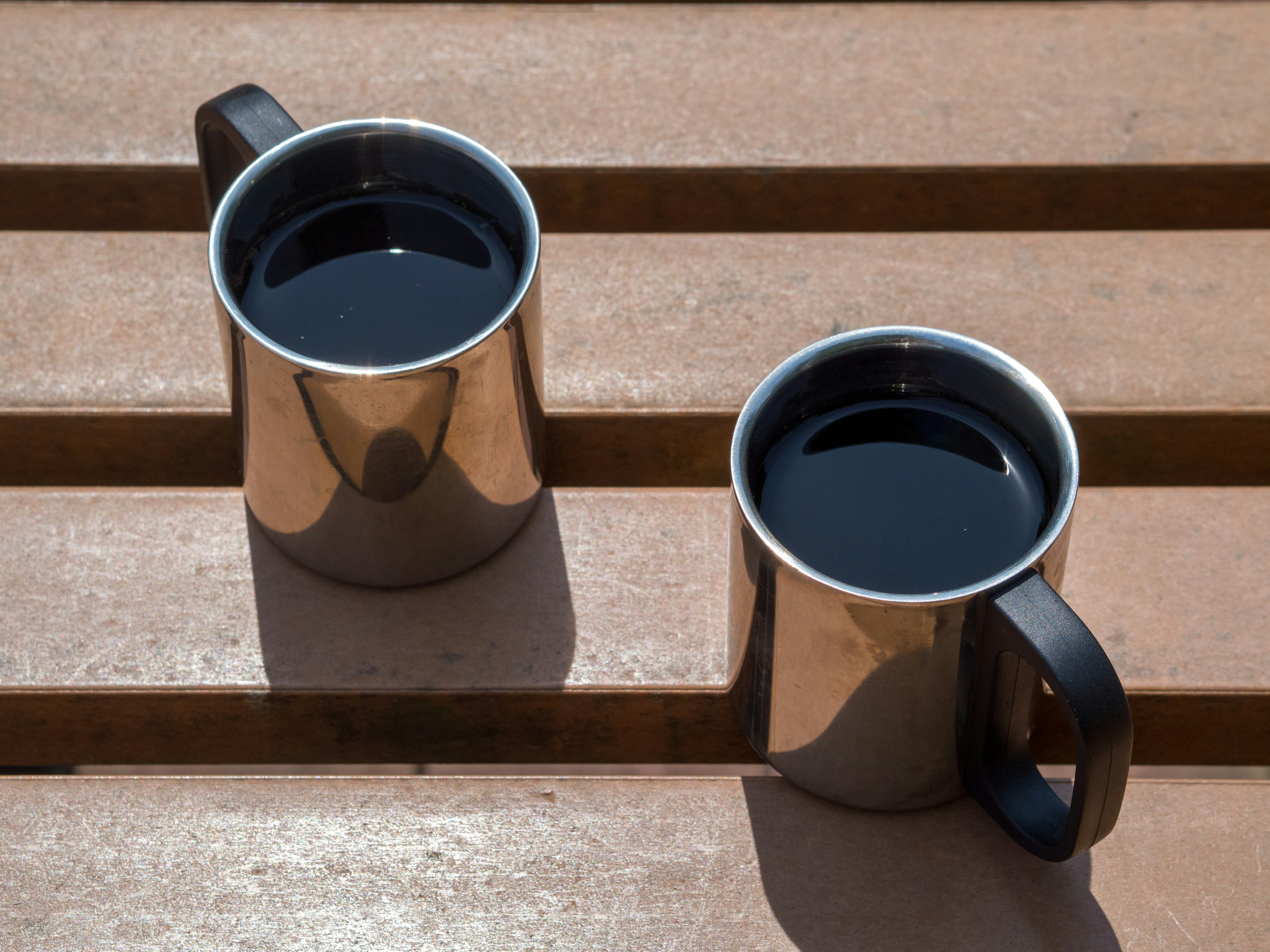 Two metallic coffee mugs on a wooden table