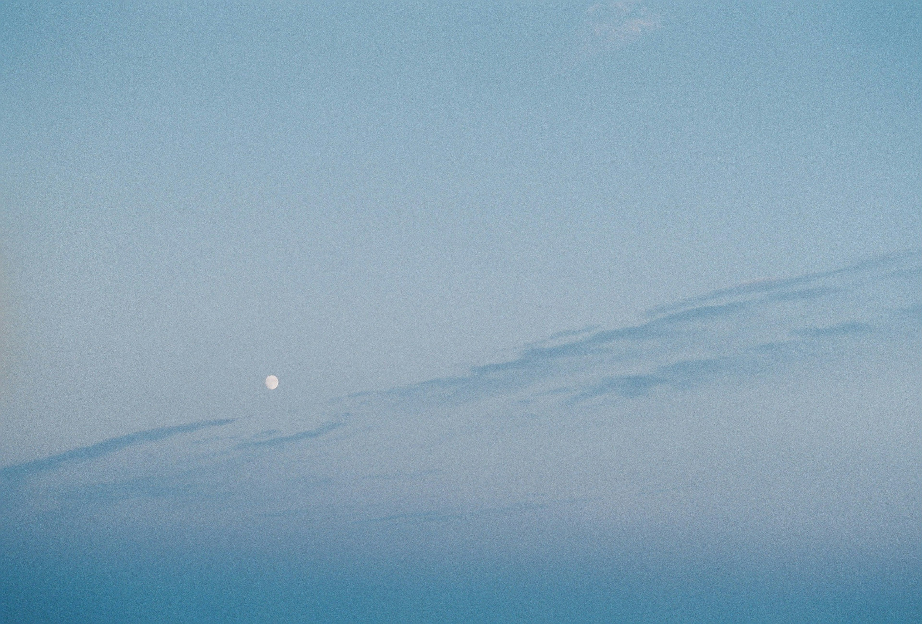 青空と雲の間に浮かぶ白い月