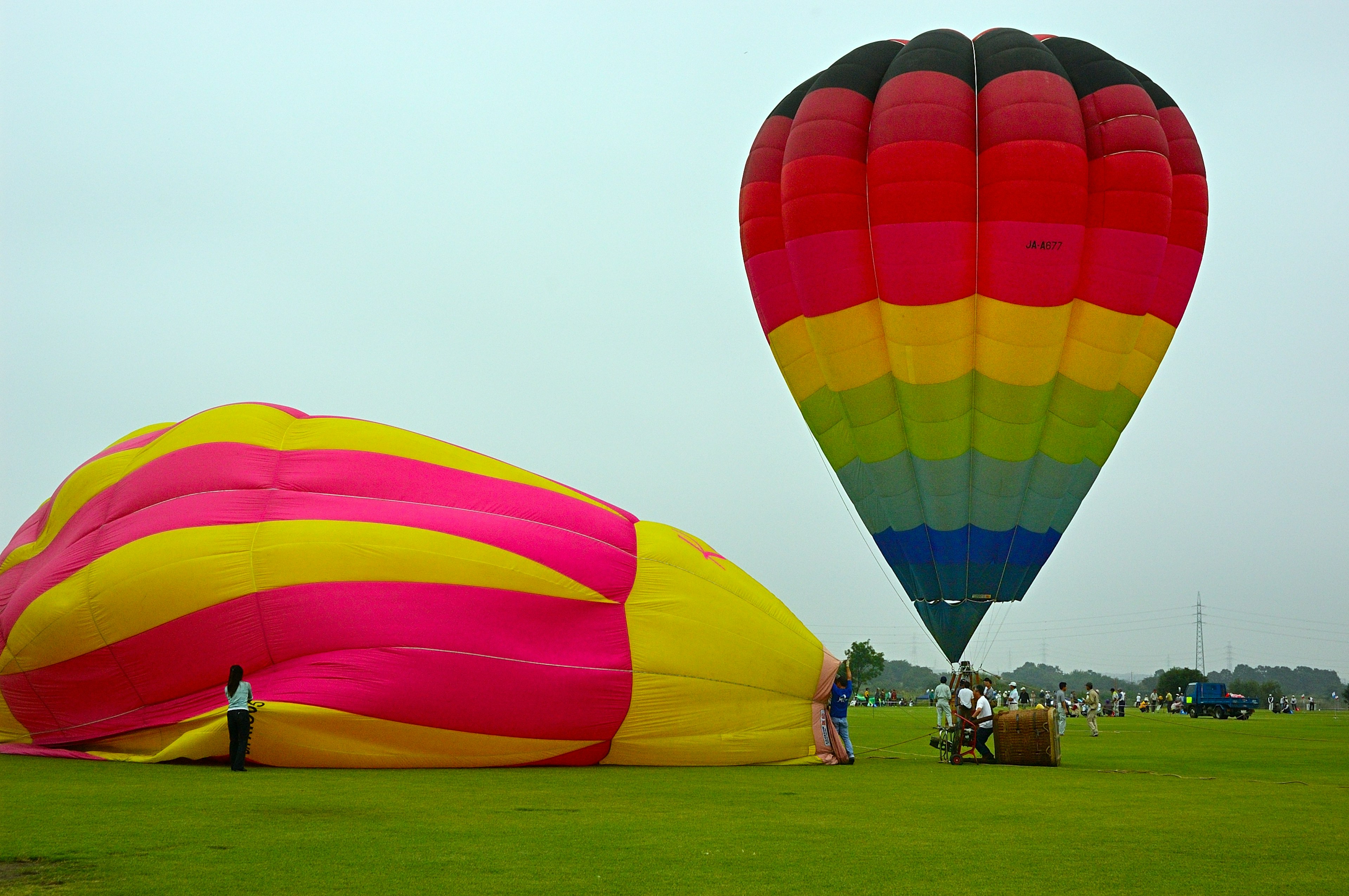 Bunte Heißluftballons an einem Startplatz Ein großer gelber und rosa Ballon neben einem schwarzen und regenbogenfarbenen Ballon