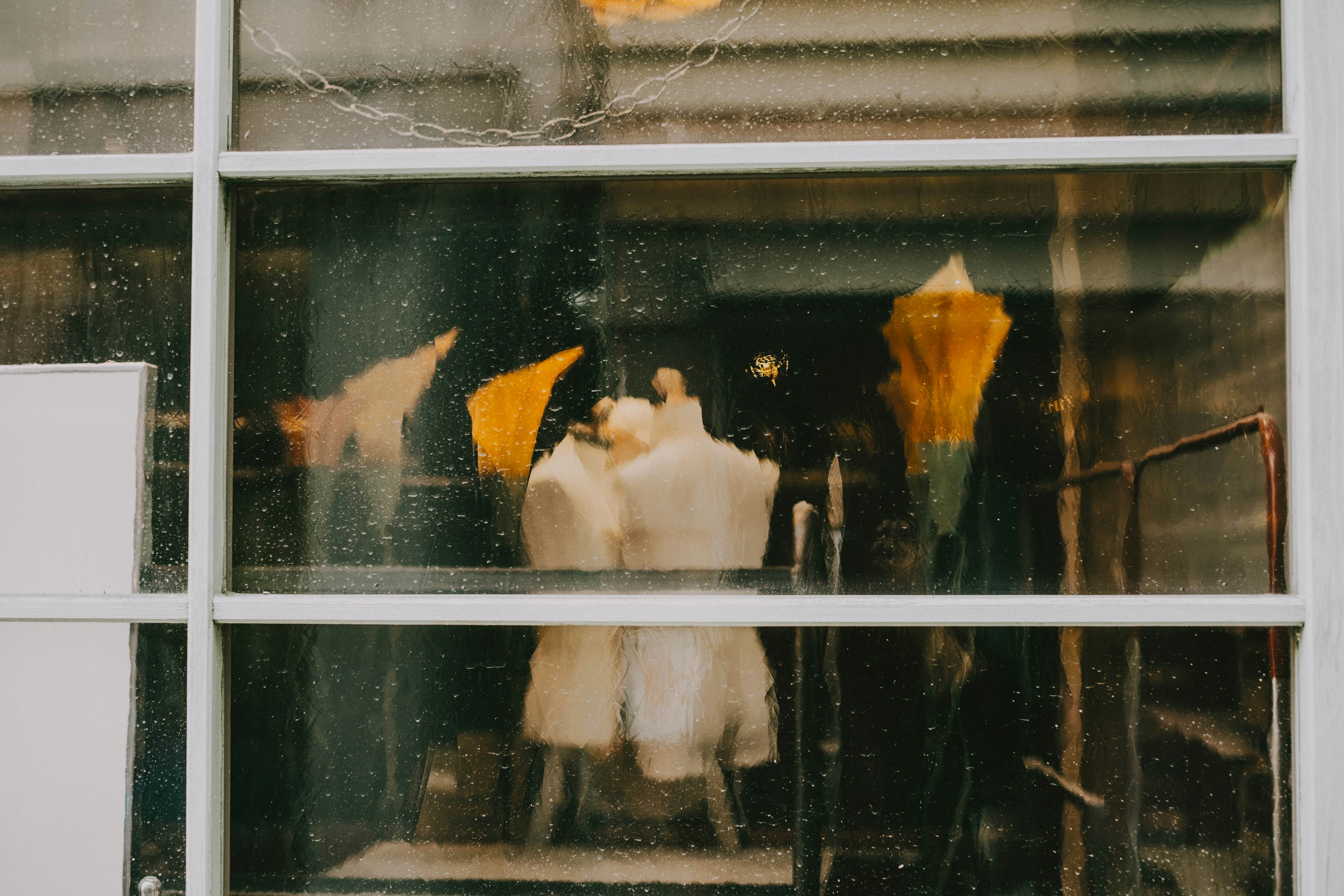 Weiße Schaufensterpuppen und bunte Regenschirme durch ein nasses Fenster gesehen