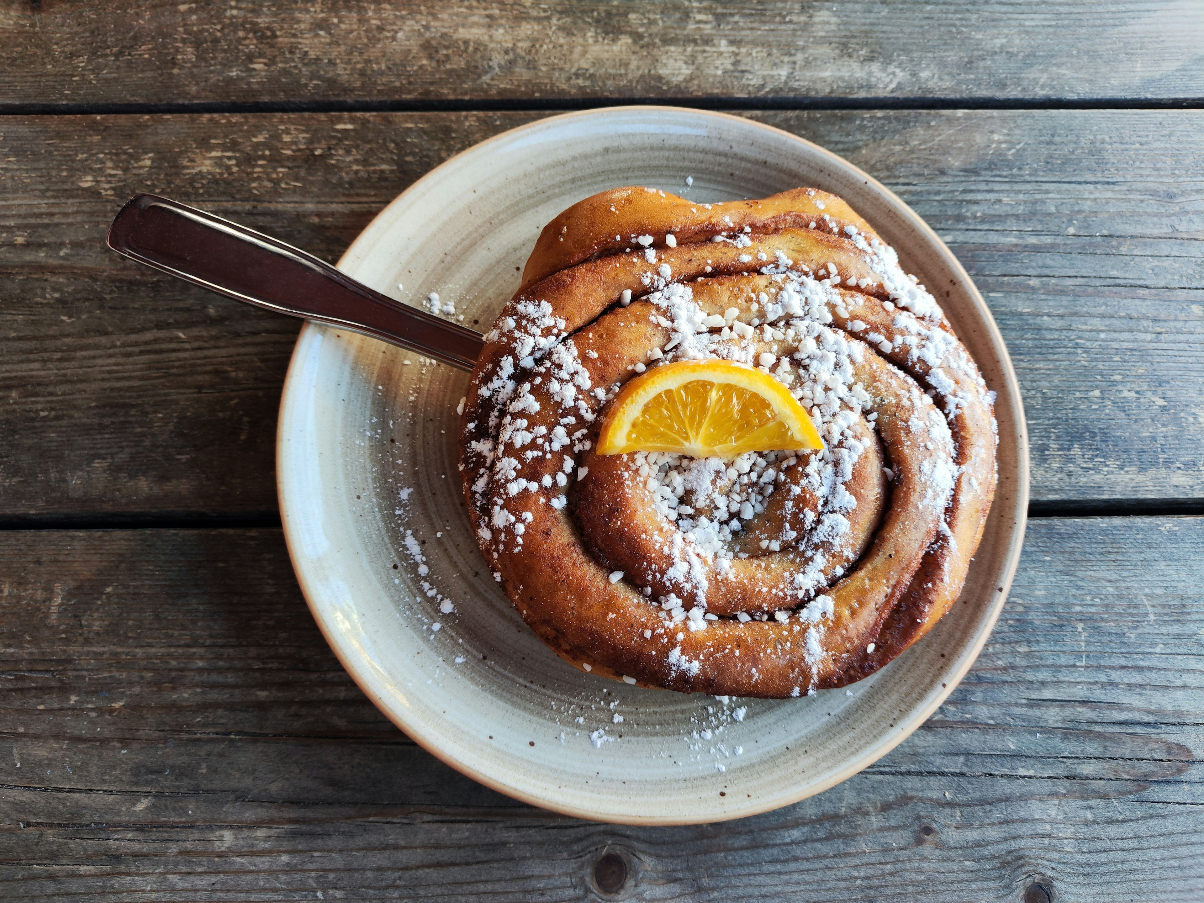 Delicious cinnamon roll topped with powdered sugar and a slice of orange on a plate