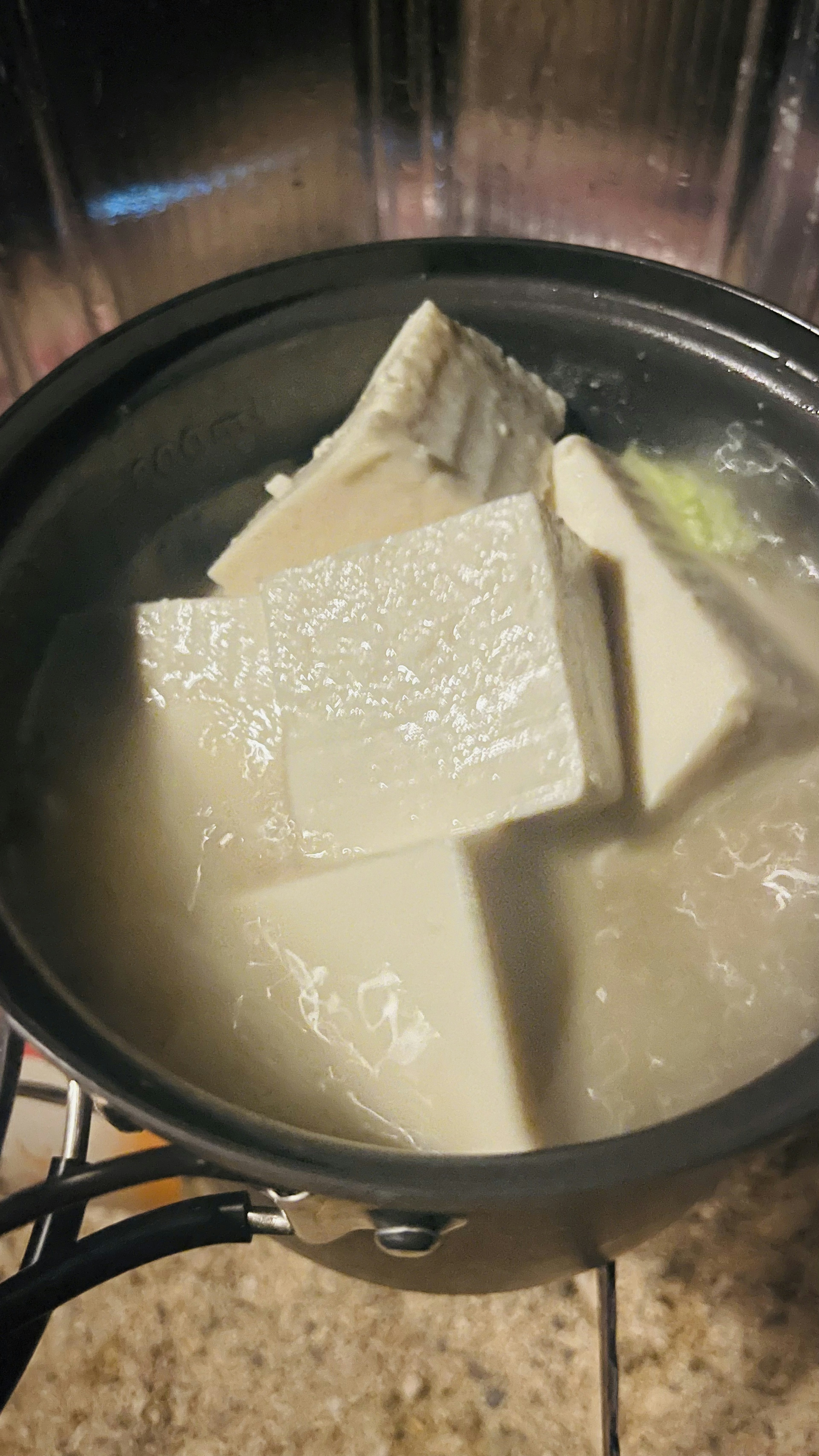 Bloques de tofu hirviendo en una olla con un líquido blanco