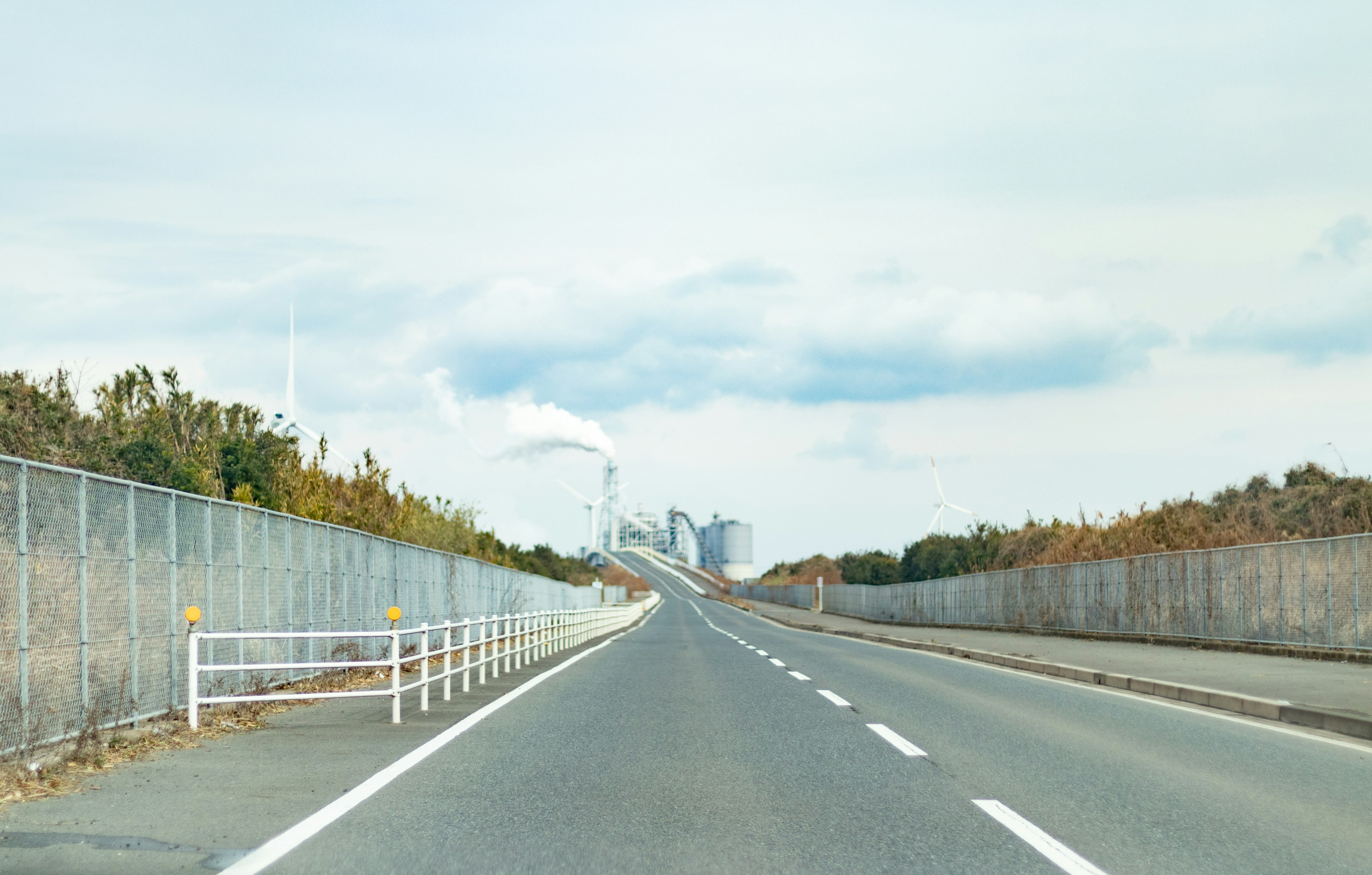 Wide road with visible factory smokestacks in the background