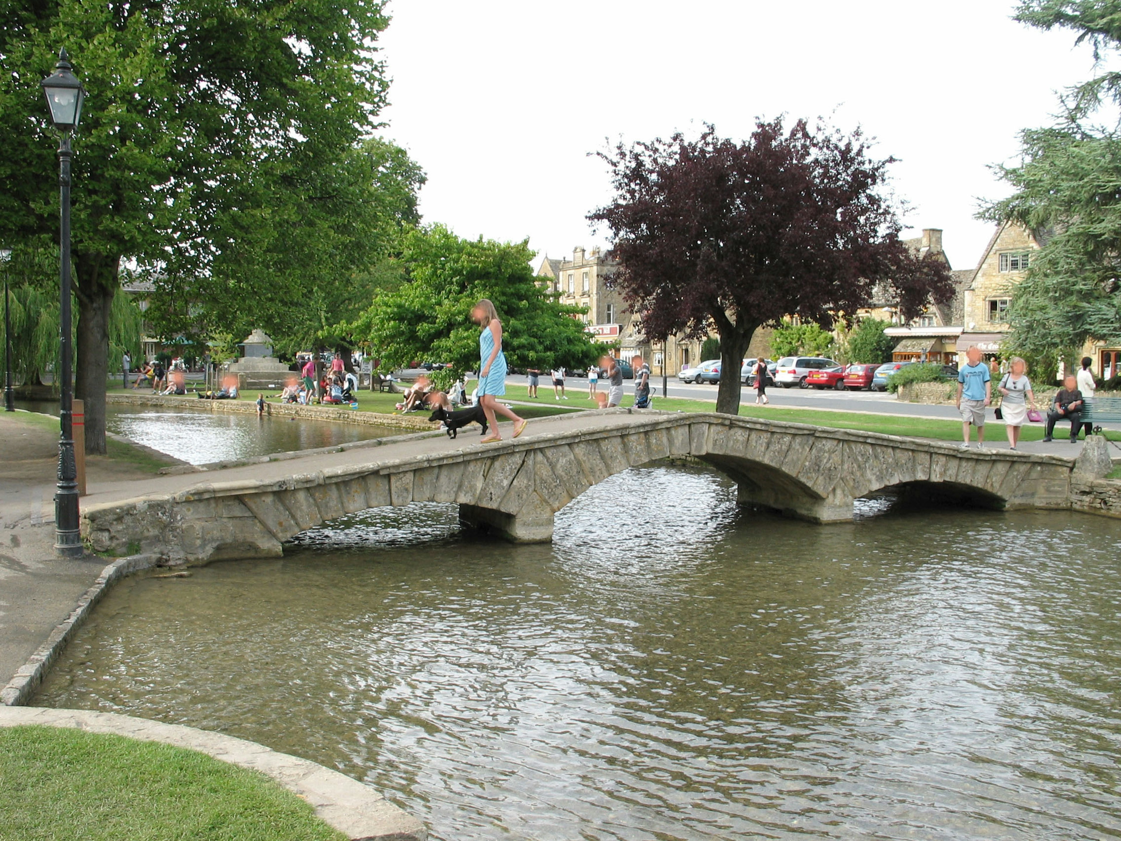 Un pequeño puente sobre un estanque en un parque con personas disfrutando del paisaje