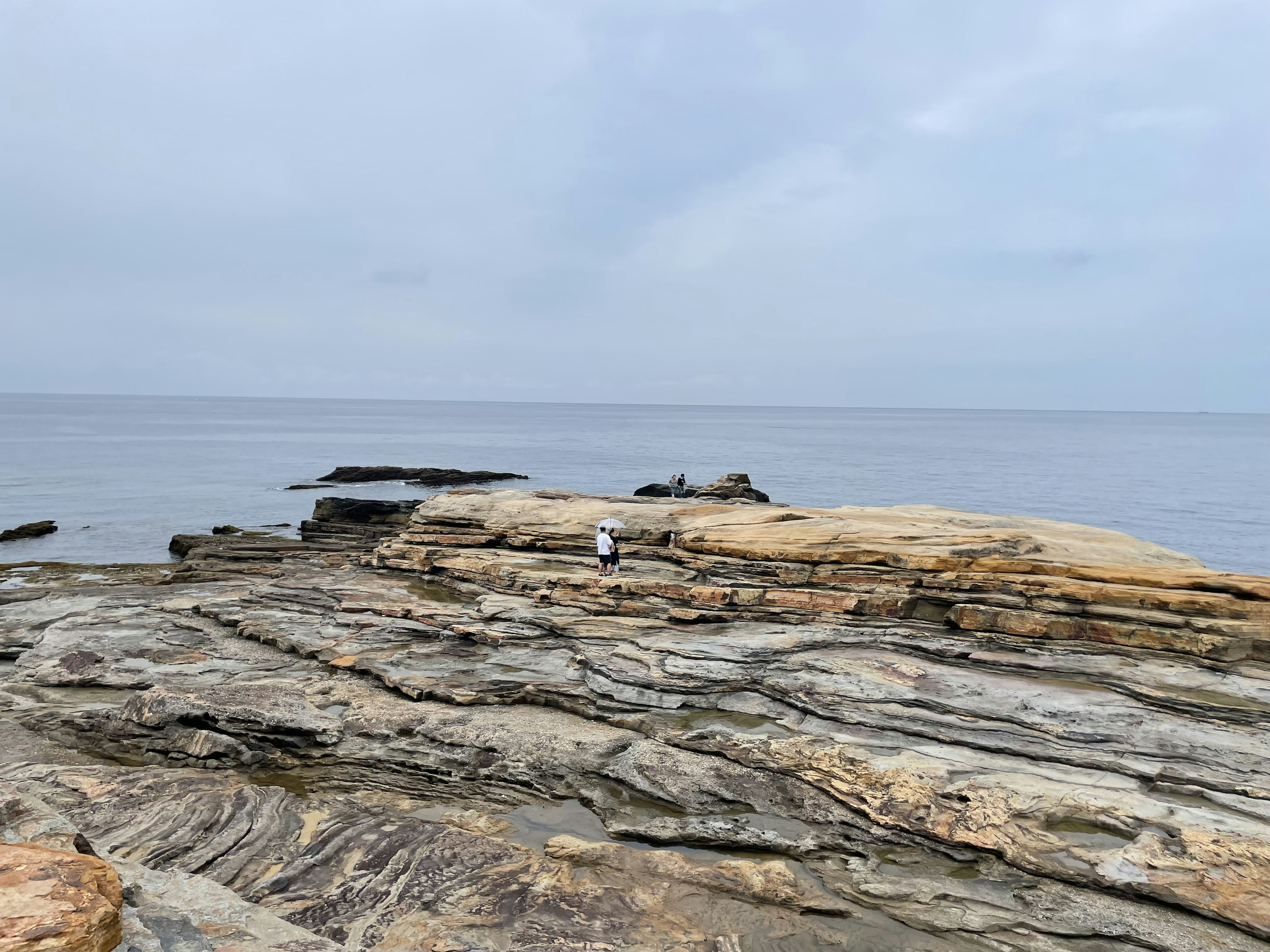 Eine Person steht auf felsigem Gelände am ruhigen Meer