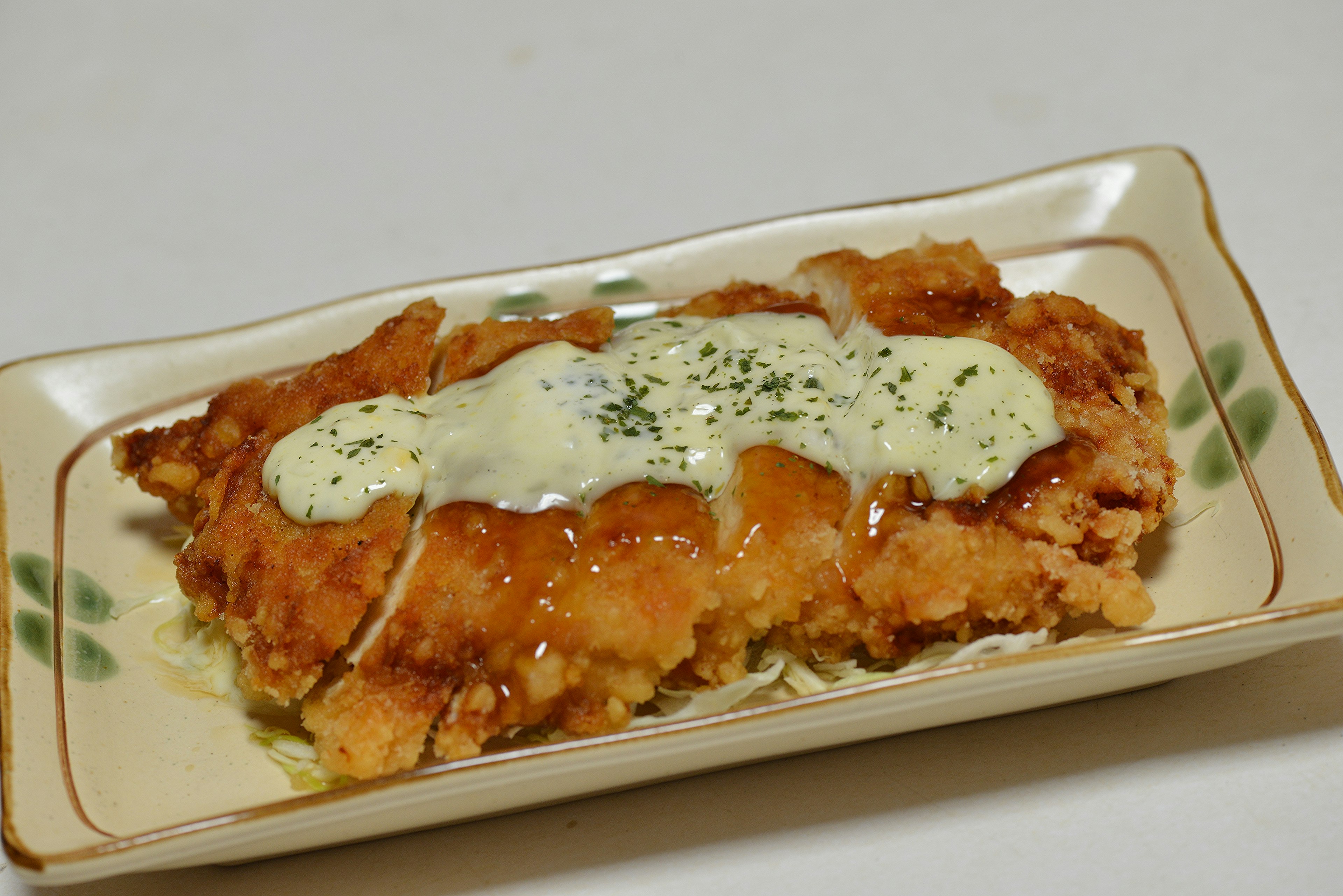 Crispy chicken topped with creamy sauce on a decorative plate