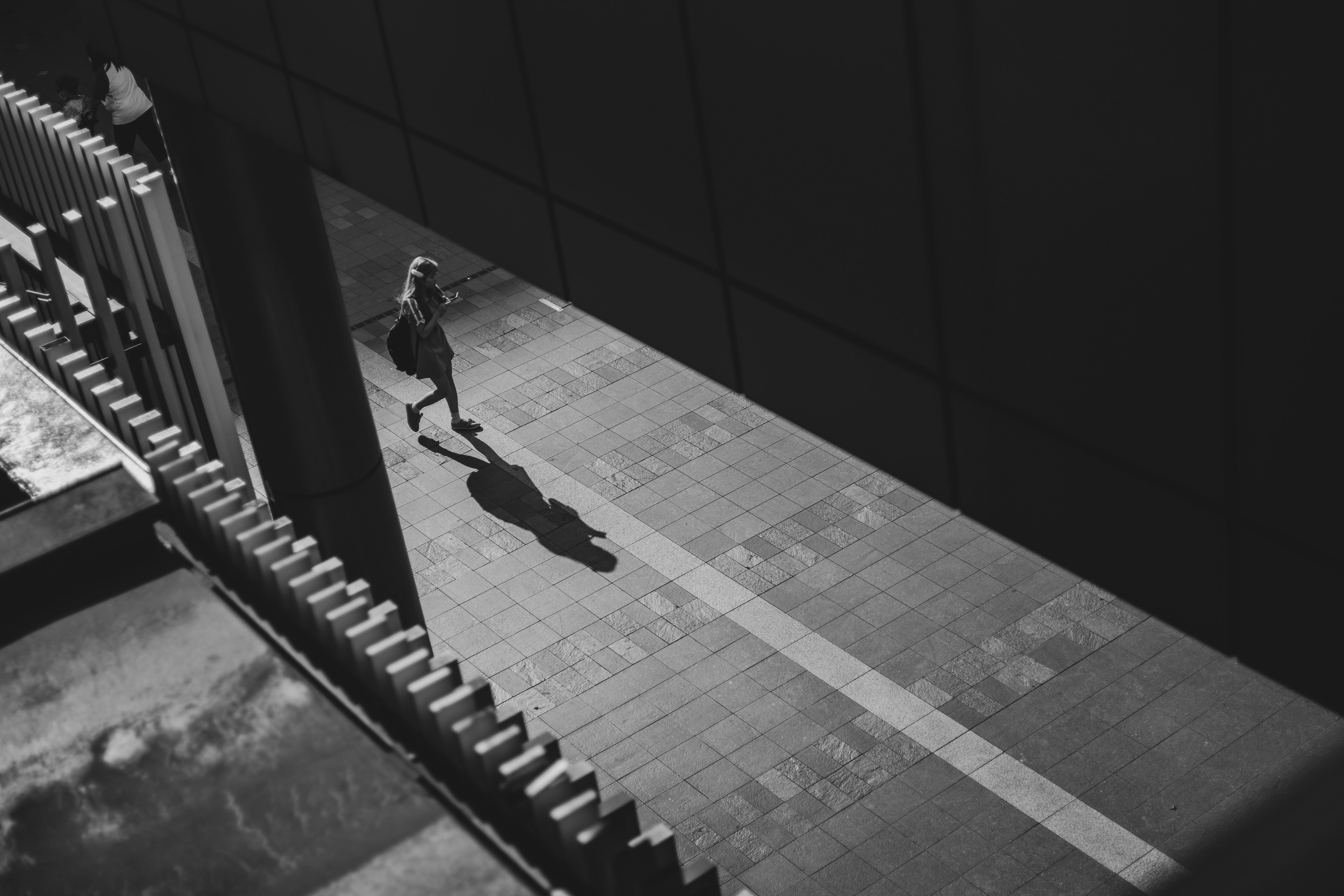 A monochrome urban scene showing a person walking with their shadow