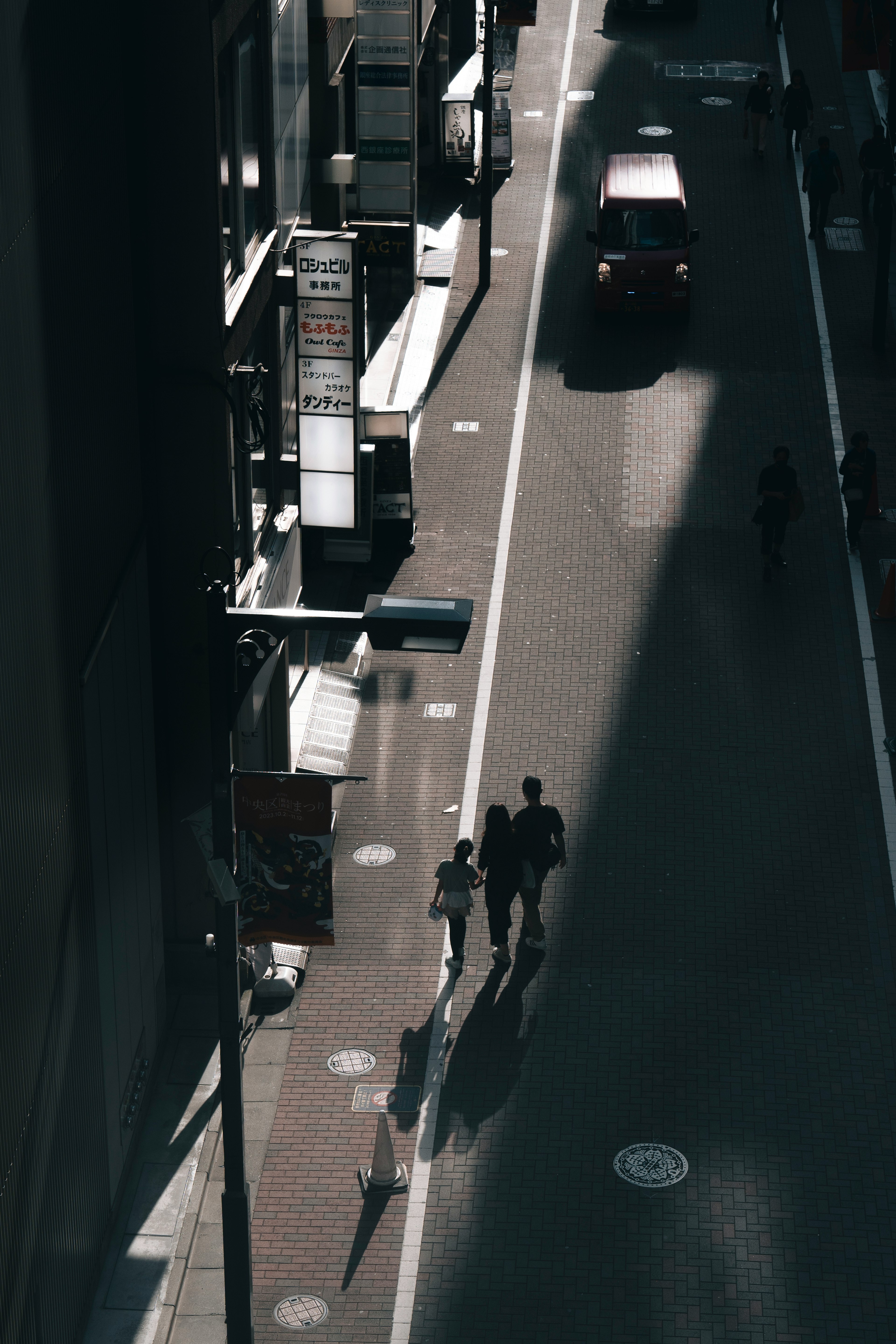 Two people walking in the shadows of a city street with a passing car