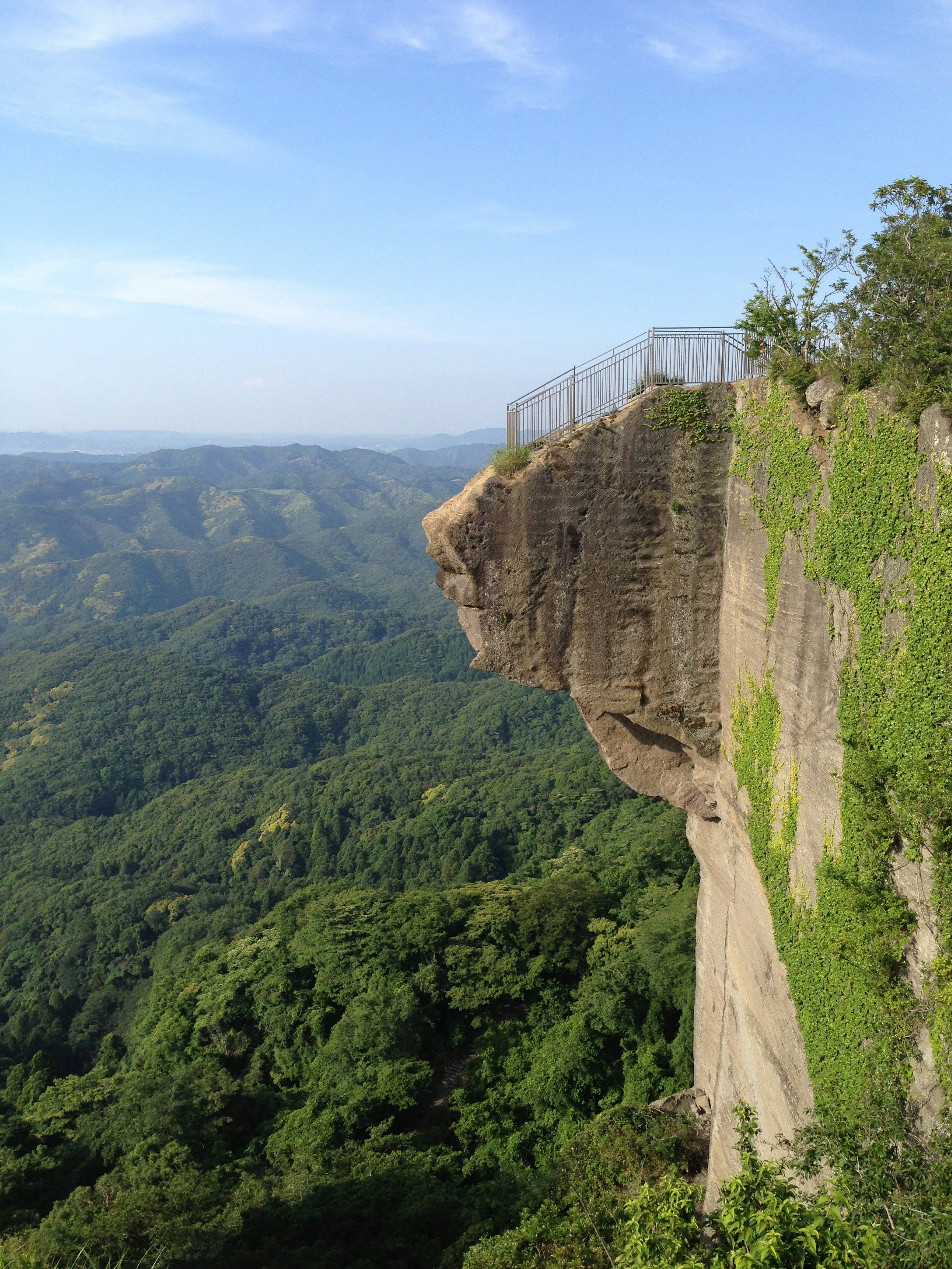 Cliff edge overlooking lush green mountains with a safety fence