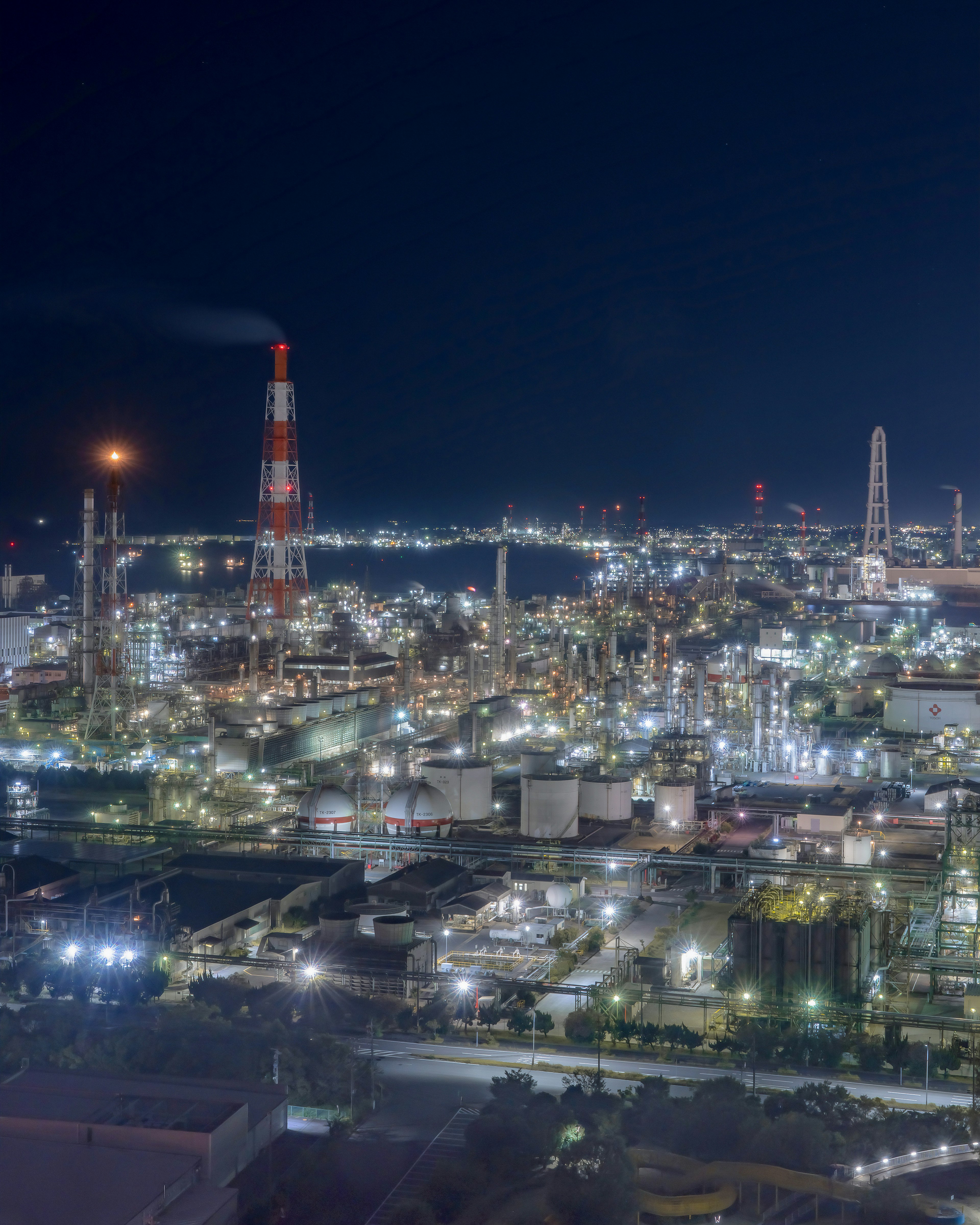 Une belle vue nocturne d'une zone industrielle avec des cheminées d'usine et des lumières brillantes