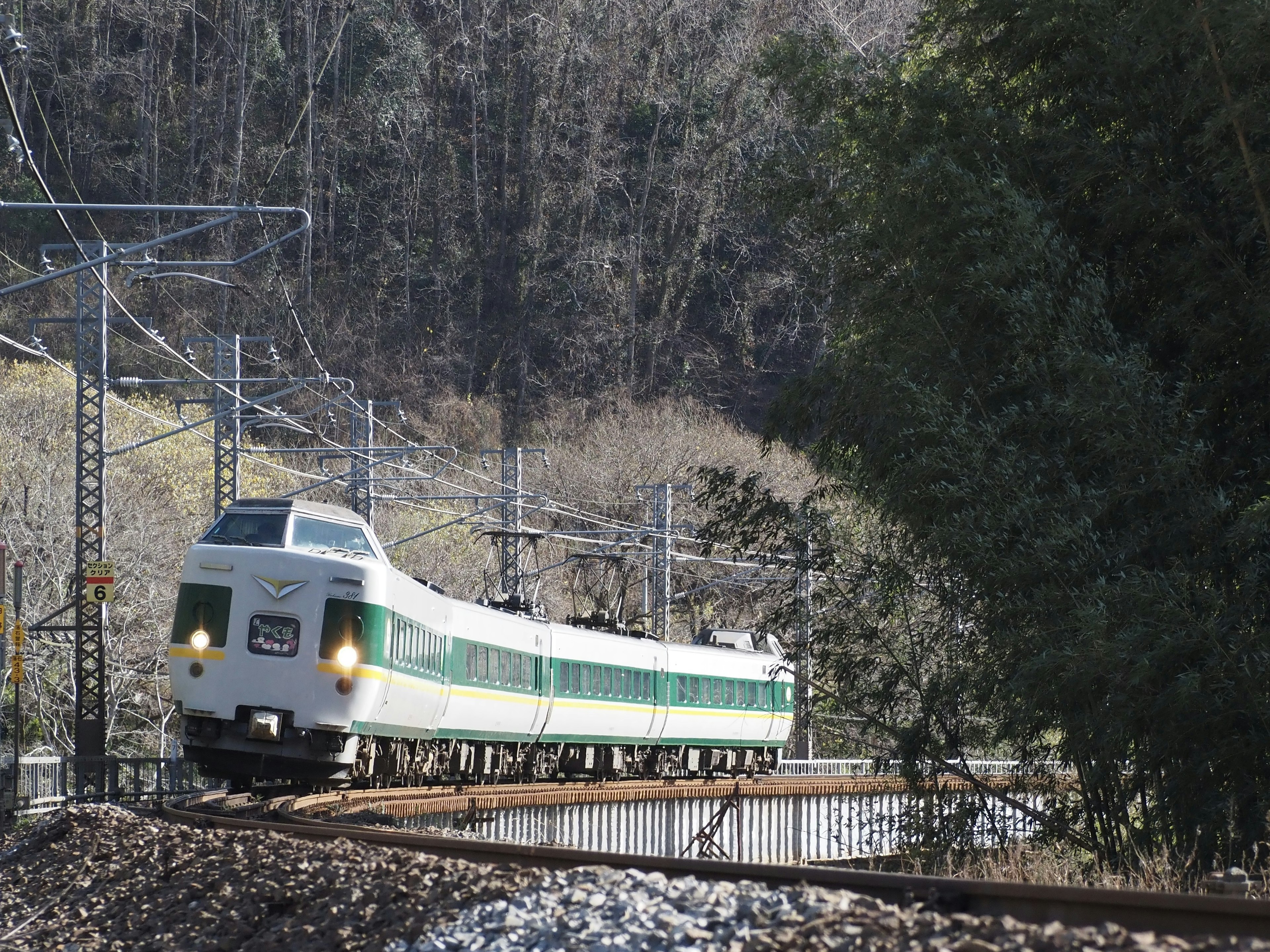 Green and white train rounding a curve in a scenic landscape