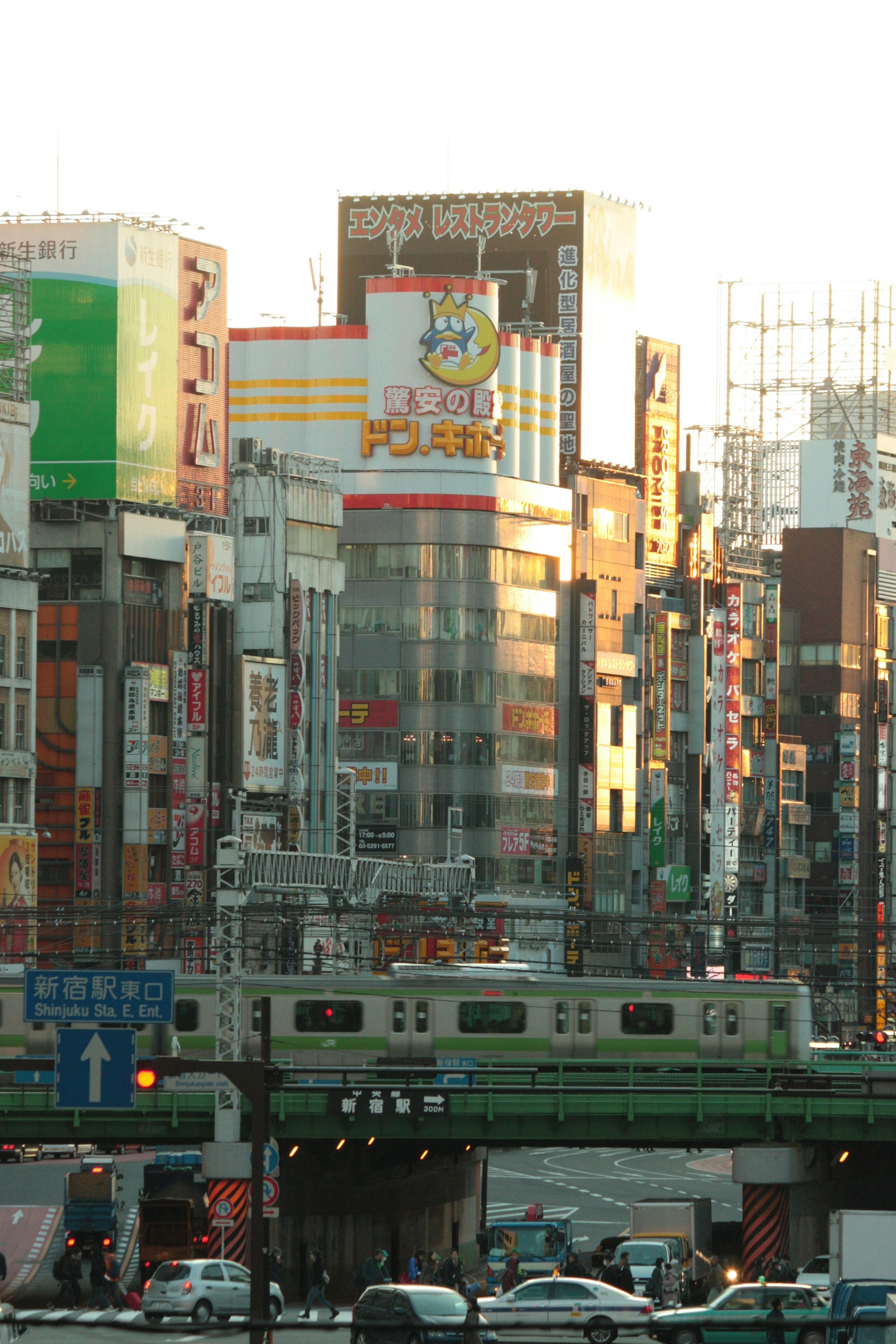 夕日を背景にした賑やかな街並みと緑の電車