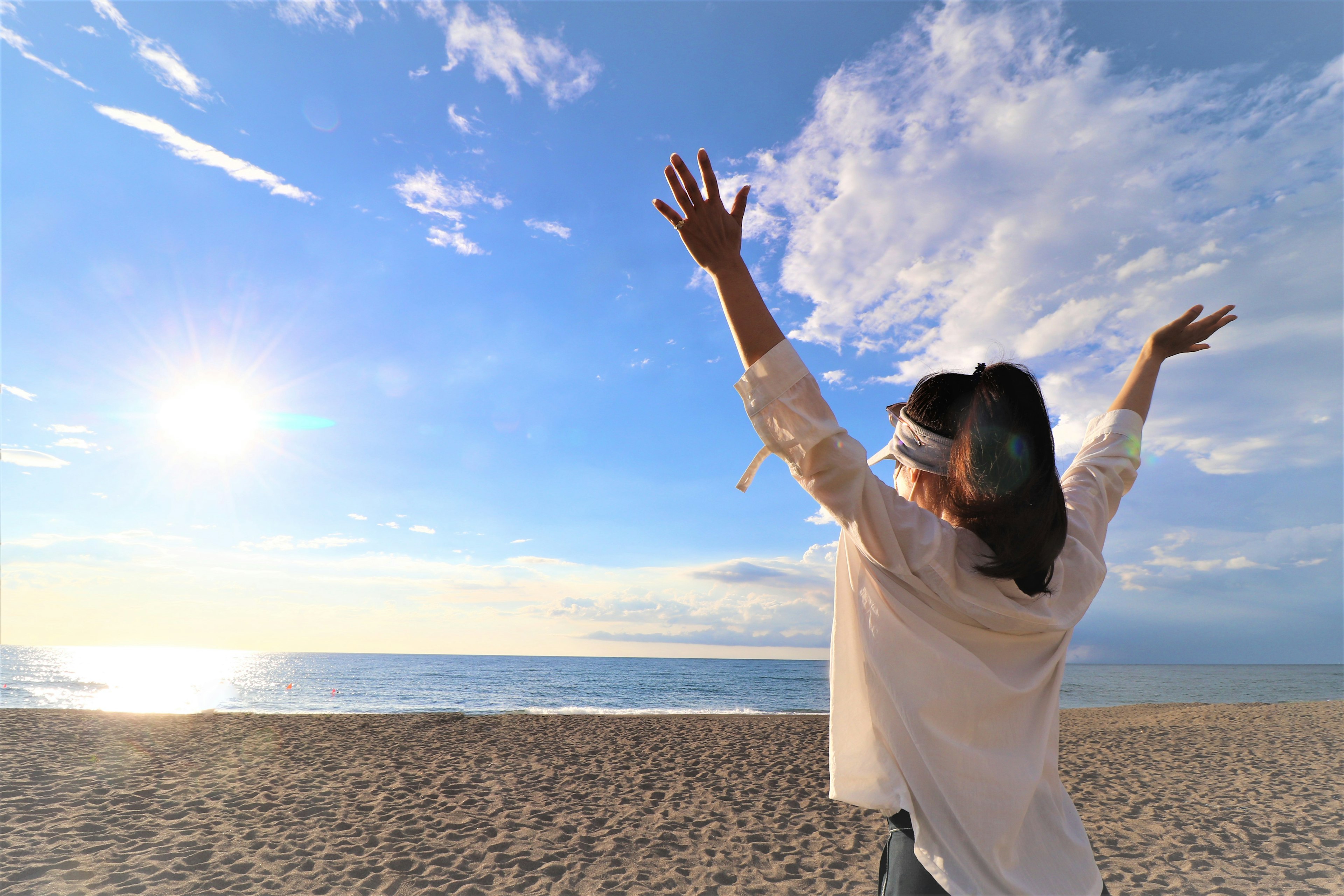 Silhouette di una donna con le braccia aperte sulla spiaggia contro un cielo blu e nuvole