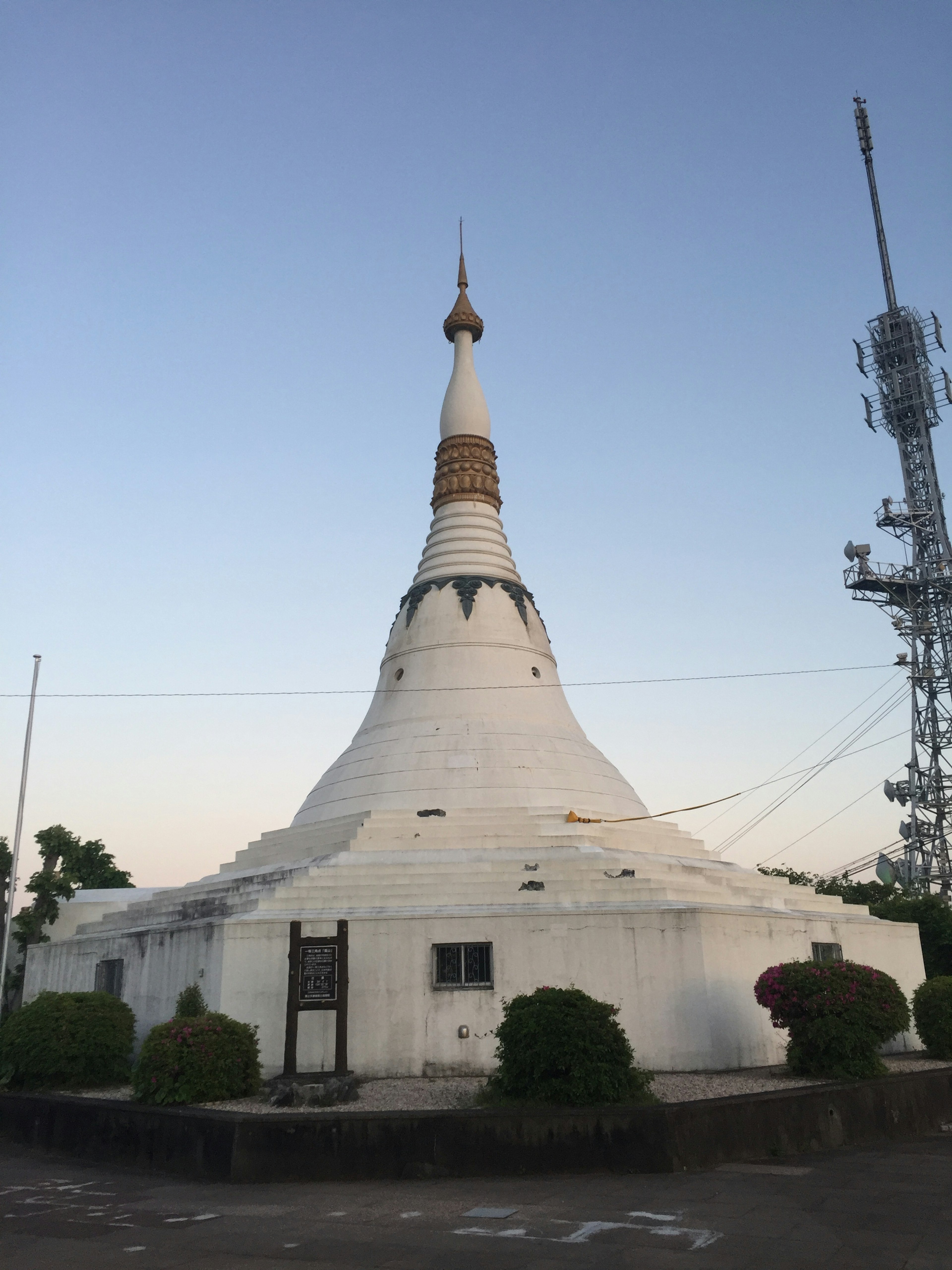 White stupa with a golden spire beside a communication tower under a twilight sky