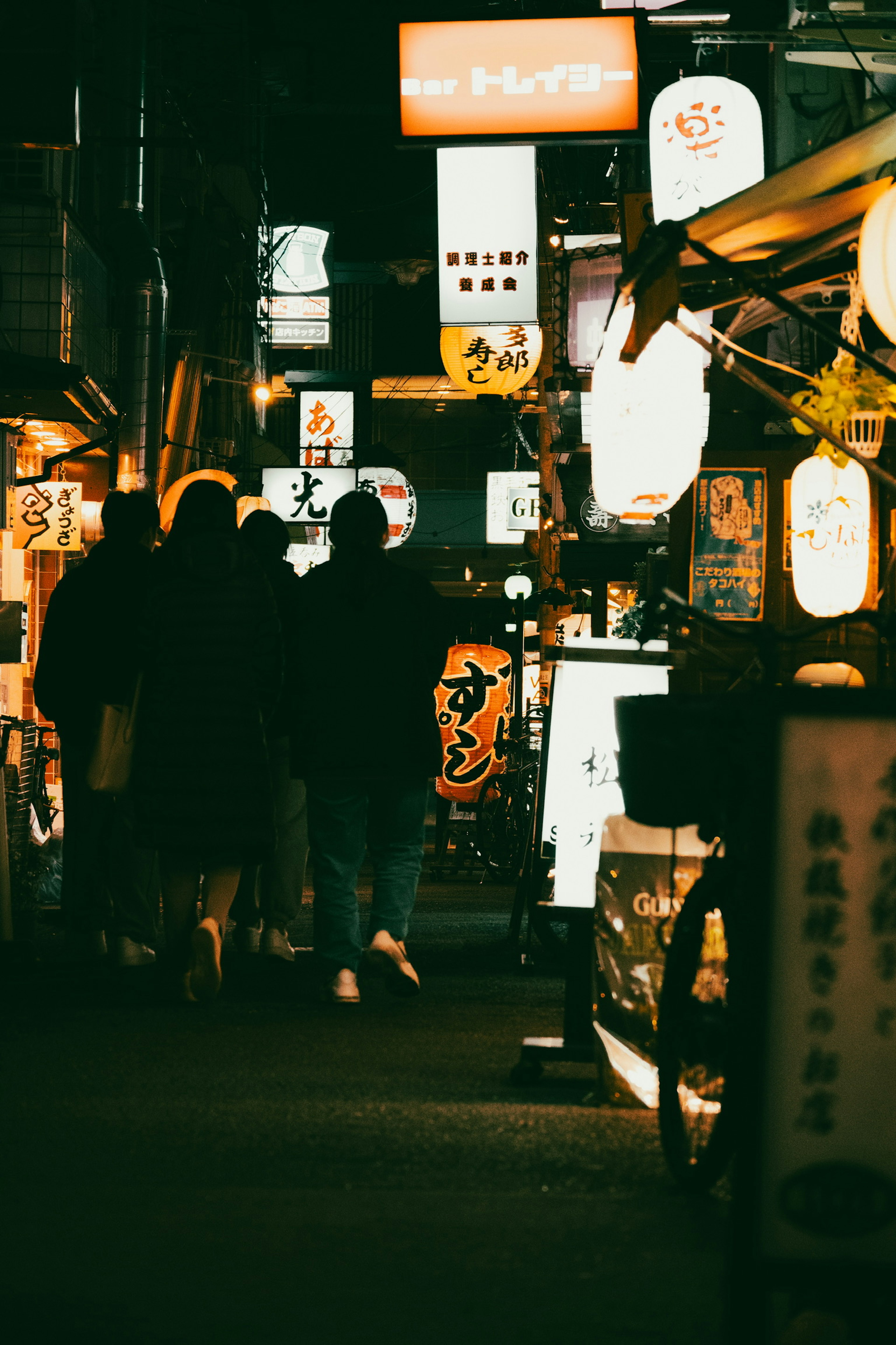 Personas caminando en una calle nocturna con letreros de restaurantes iluminados