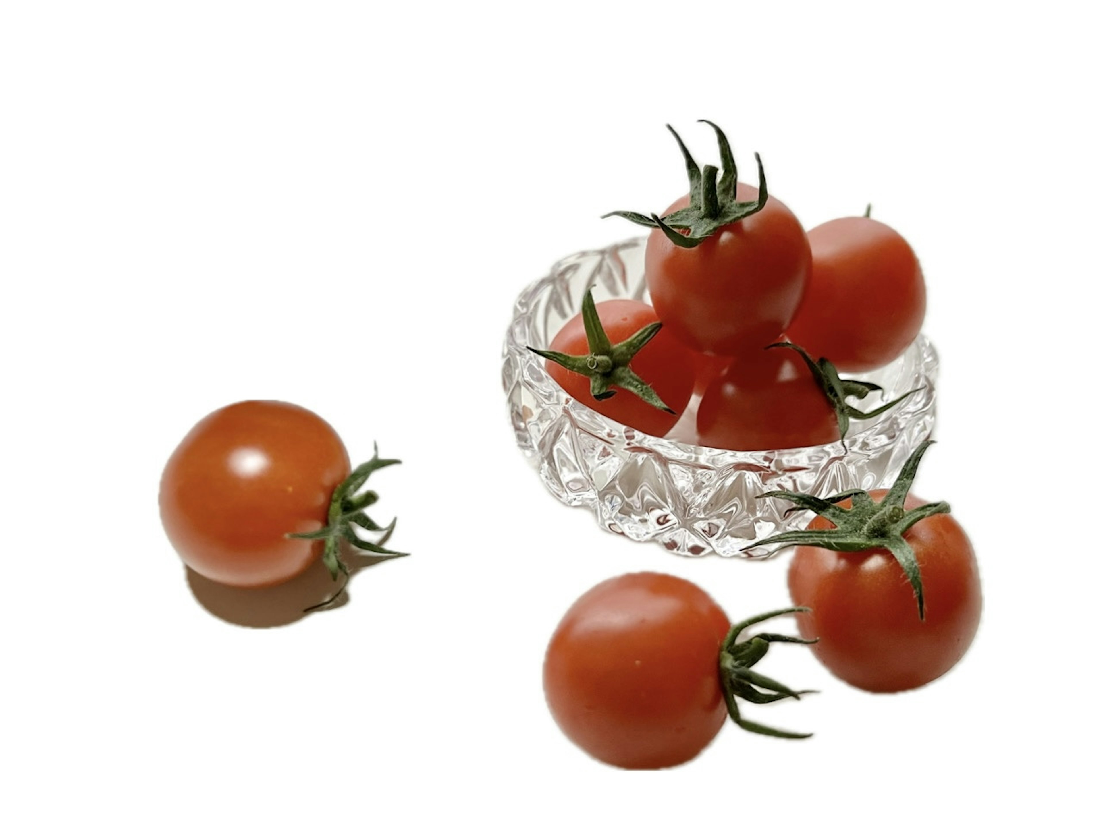 Tomates rouges dans un bol transparent avec d'autres tomates éparpillées autour