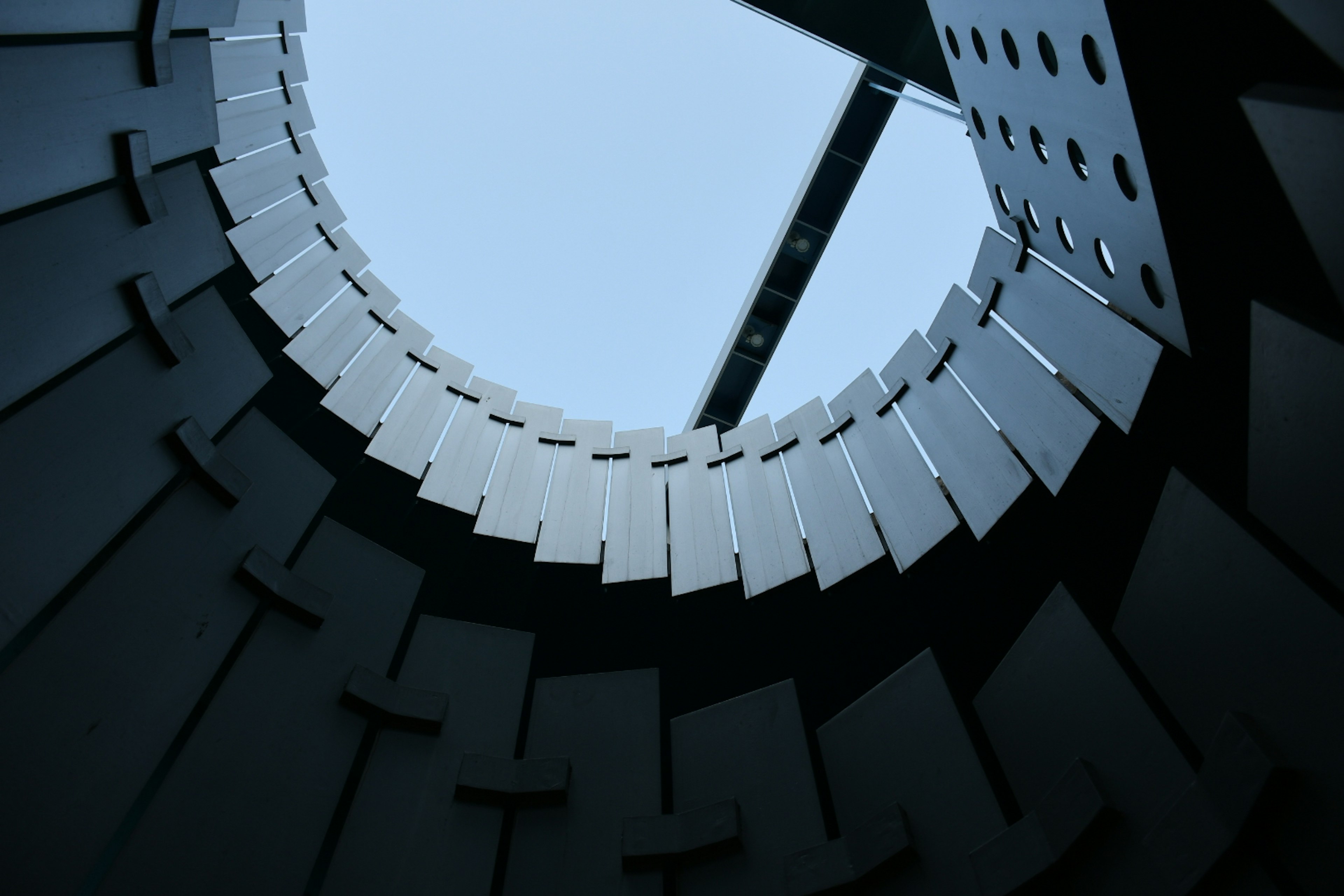 View from inside a black spiral staircase looking up at the blue sky