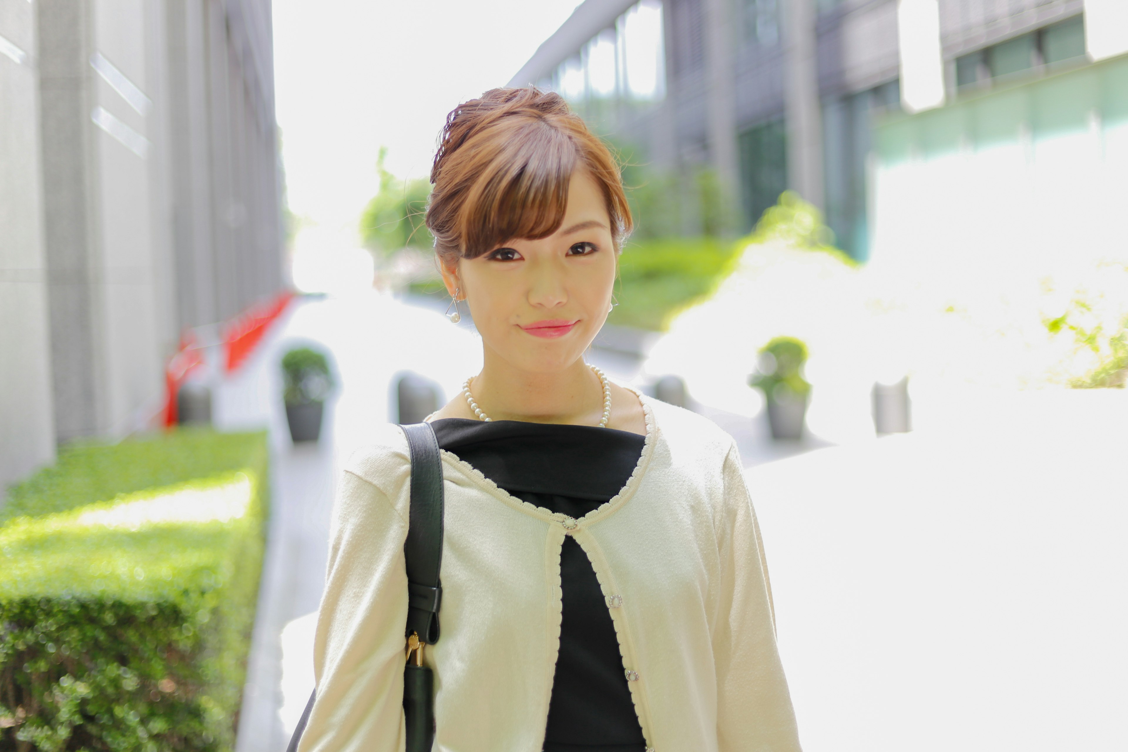 A smiling woman in a beige jacket standing outdoors in bright light