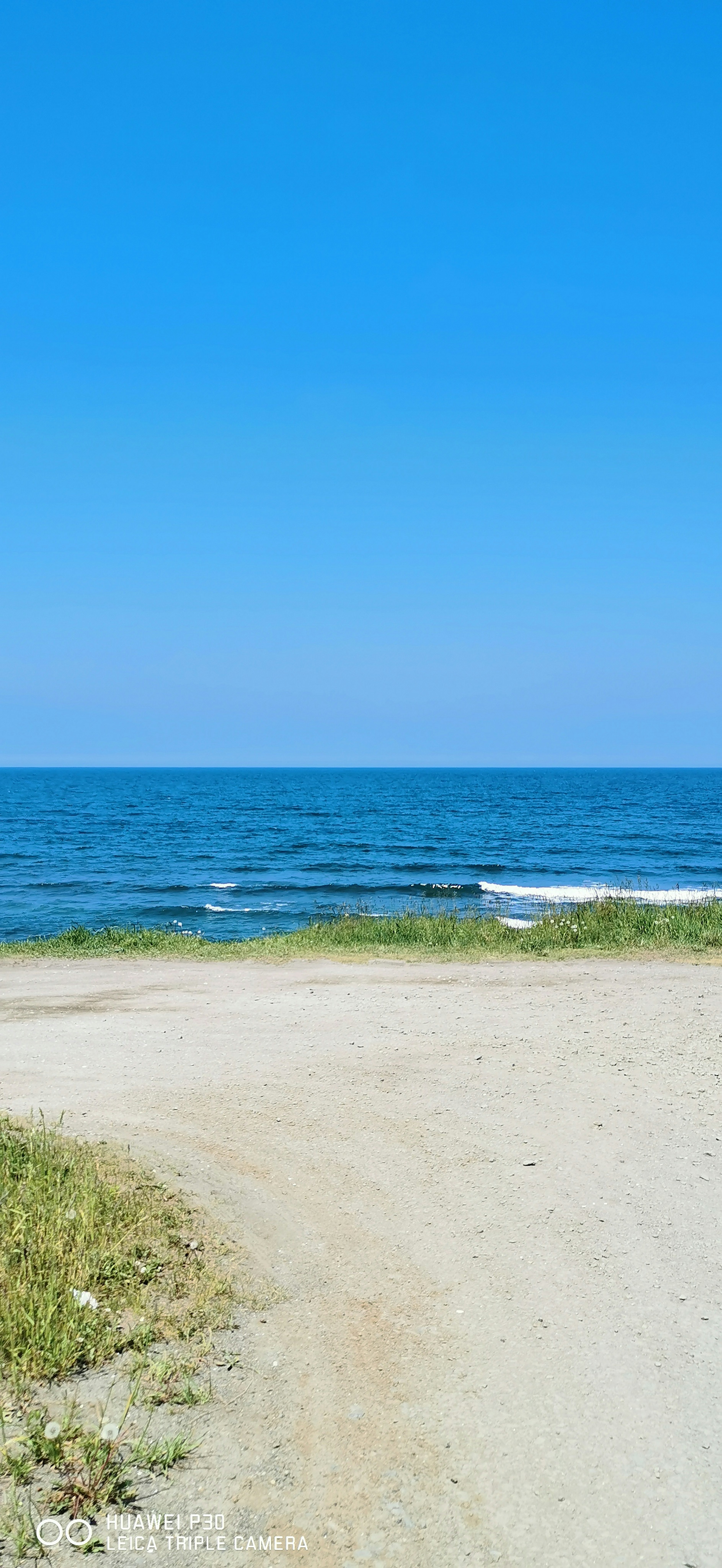 Scenic view of a blue sky and ocean with a sandy path leading to the water