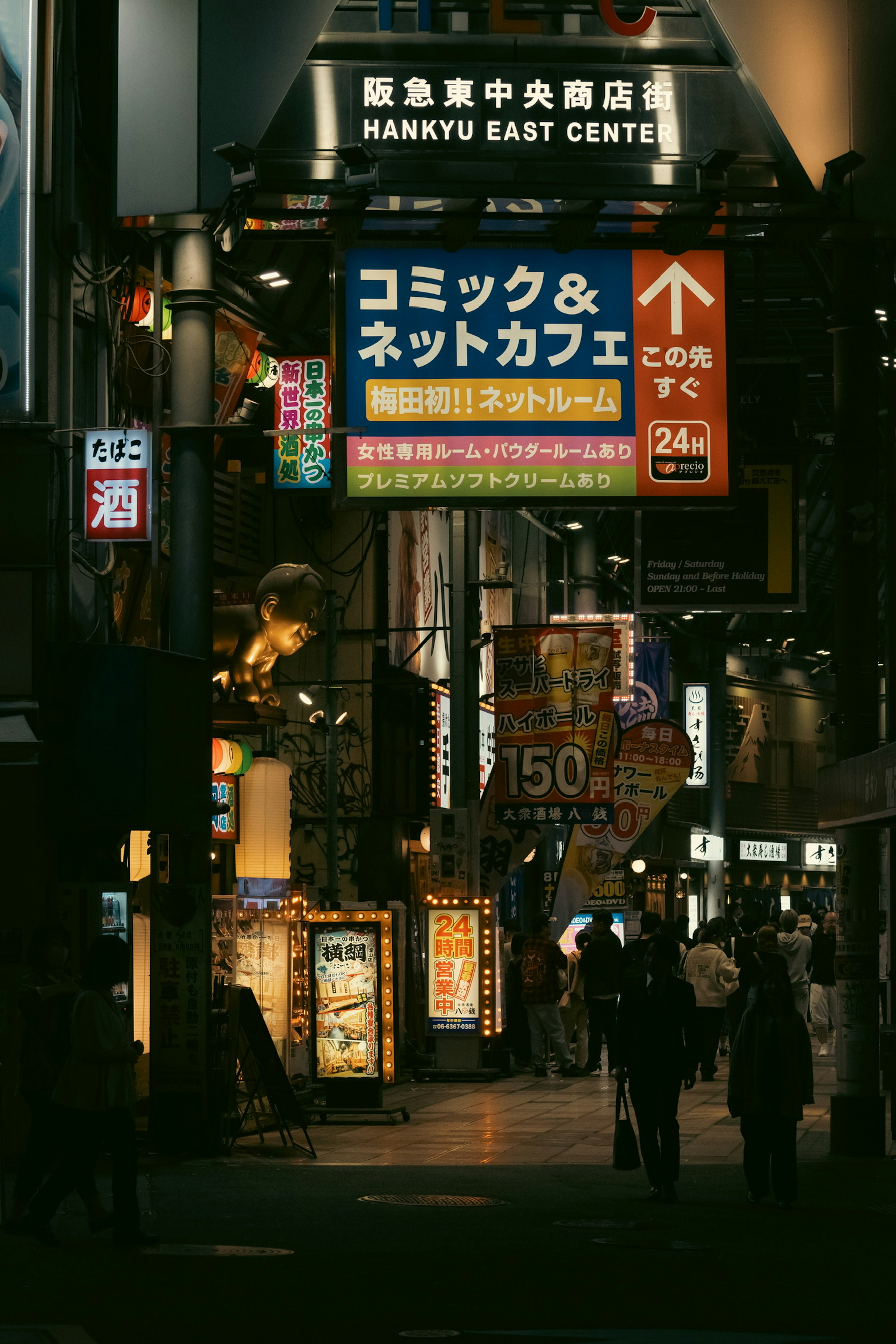 Night scene of a bustling street with illuminated signs featuring a comic and net café