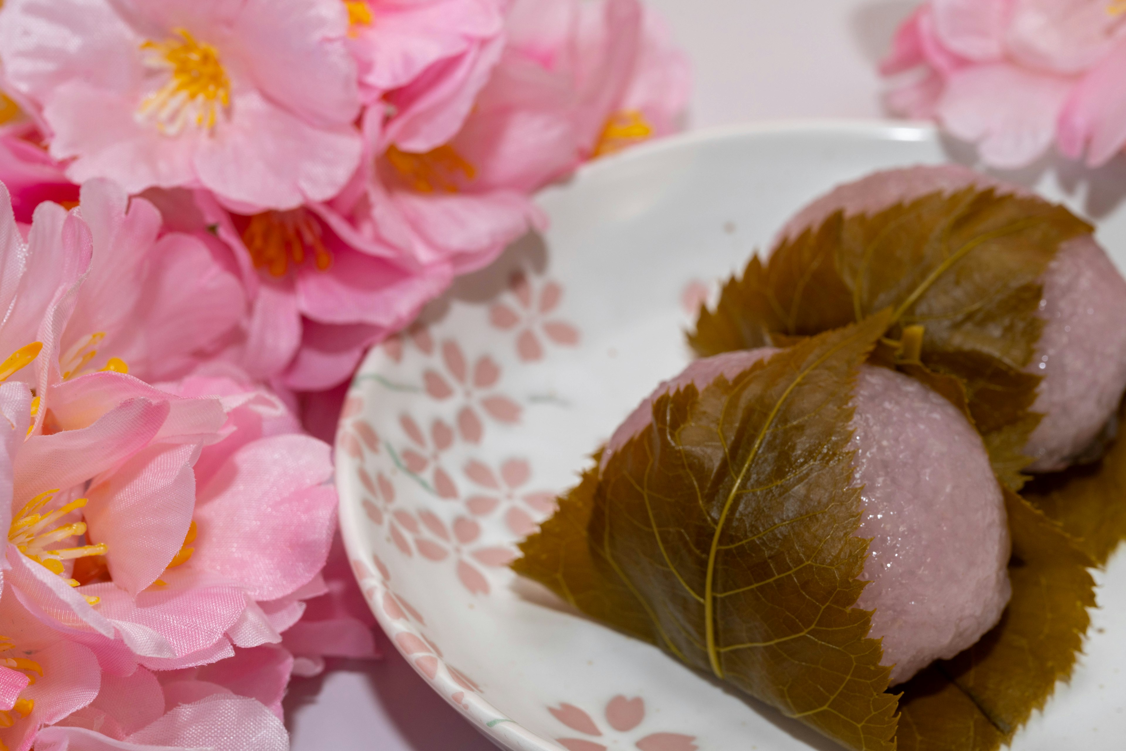 Piring kue Jepang yang dibungkus daun di samping bunga sakura pink