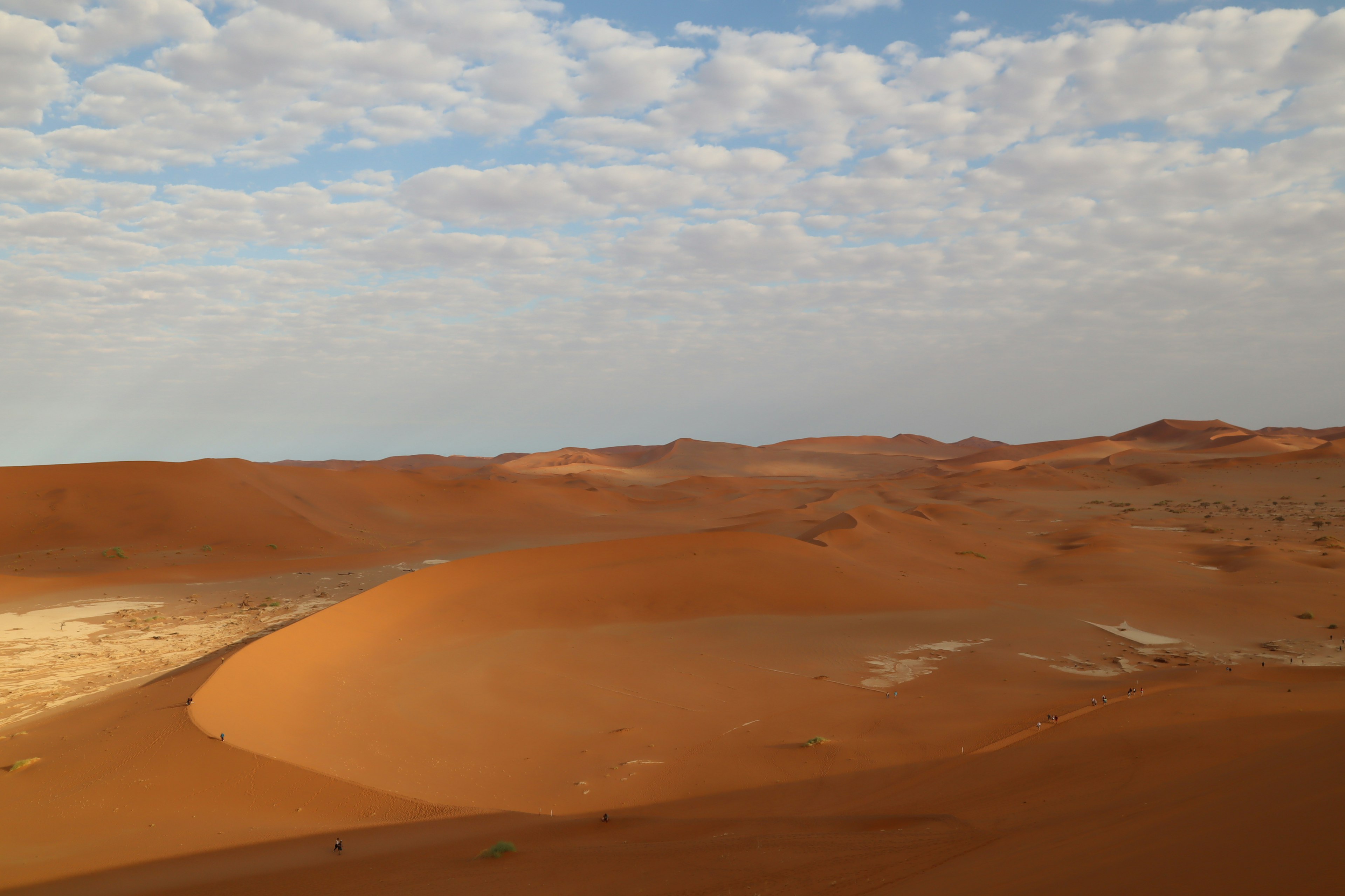 Expansive orange sand dunes under a blue sky with clouds