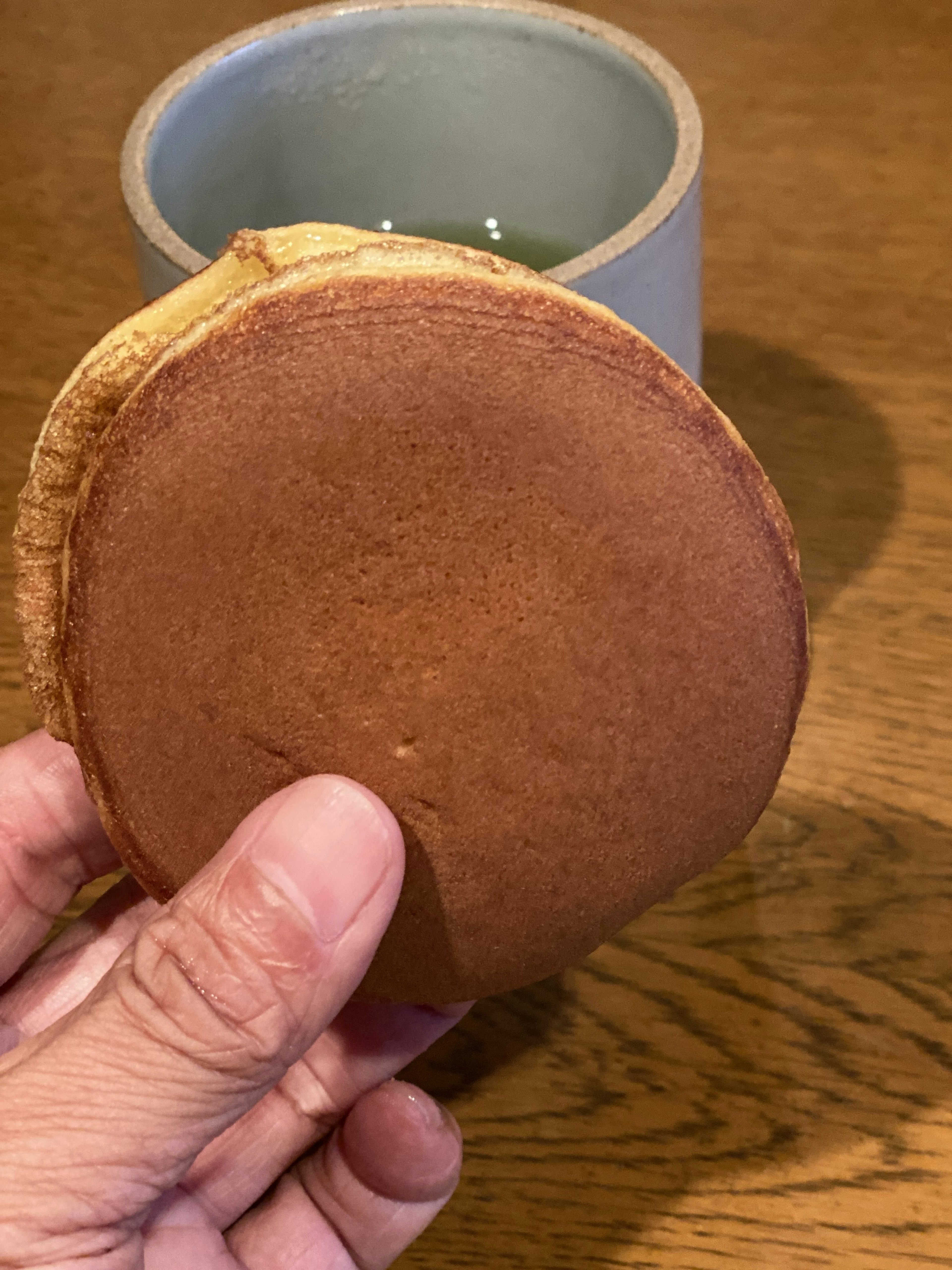 手に持たれた和菓子のような丸いお菓子と背景の緑色のカップ