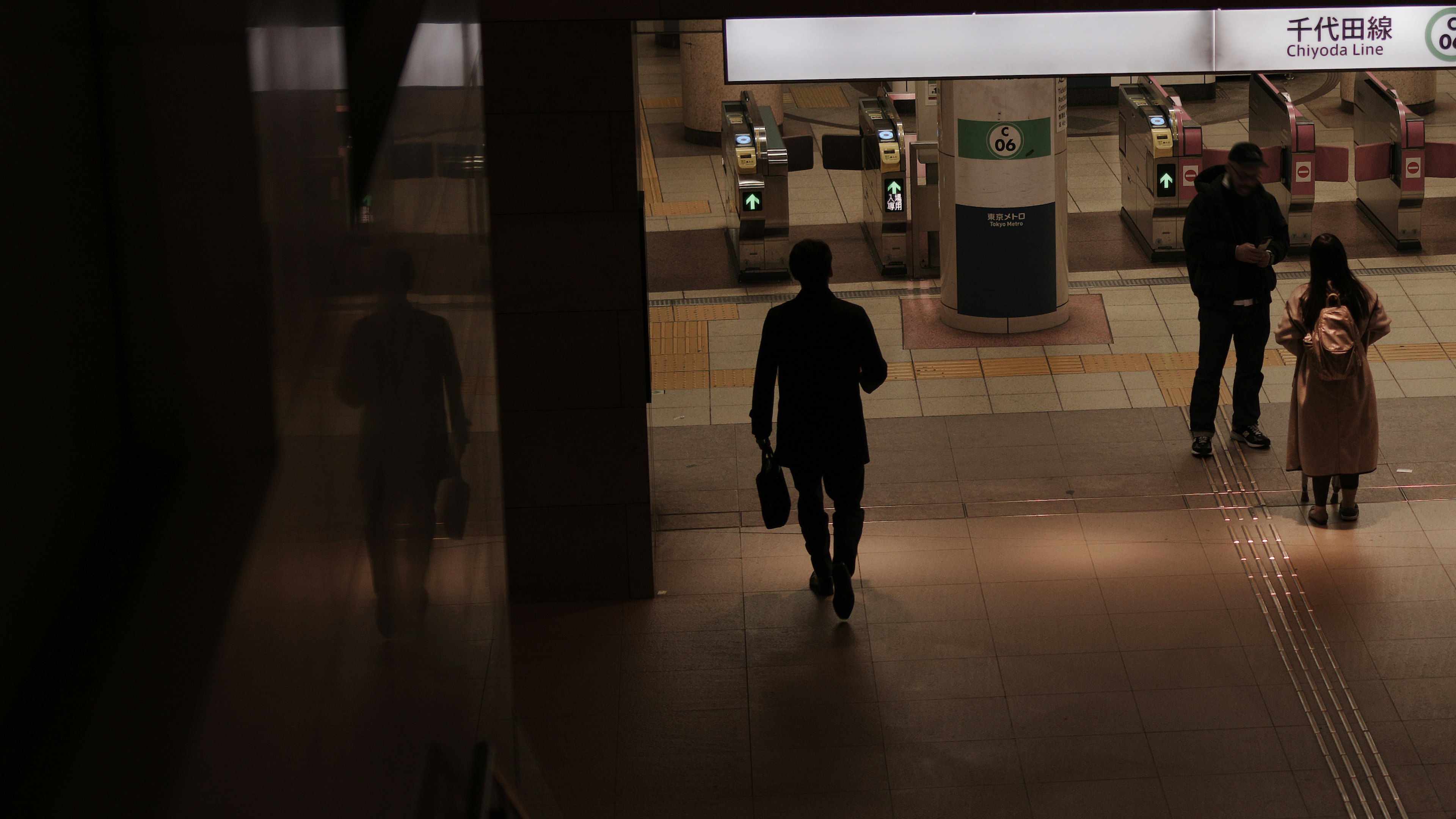 暗い駅の通路を歩く男性と他の乗客の姿