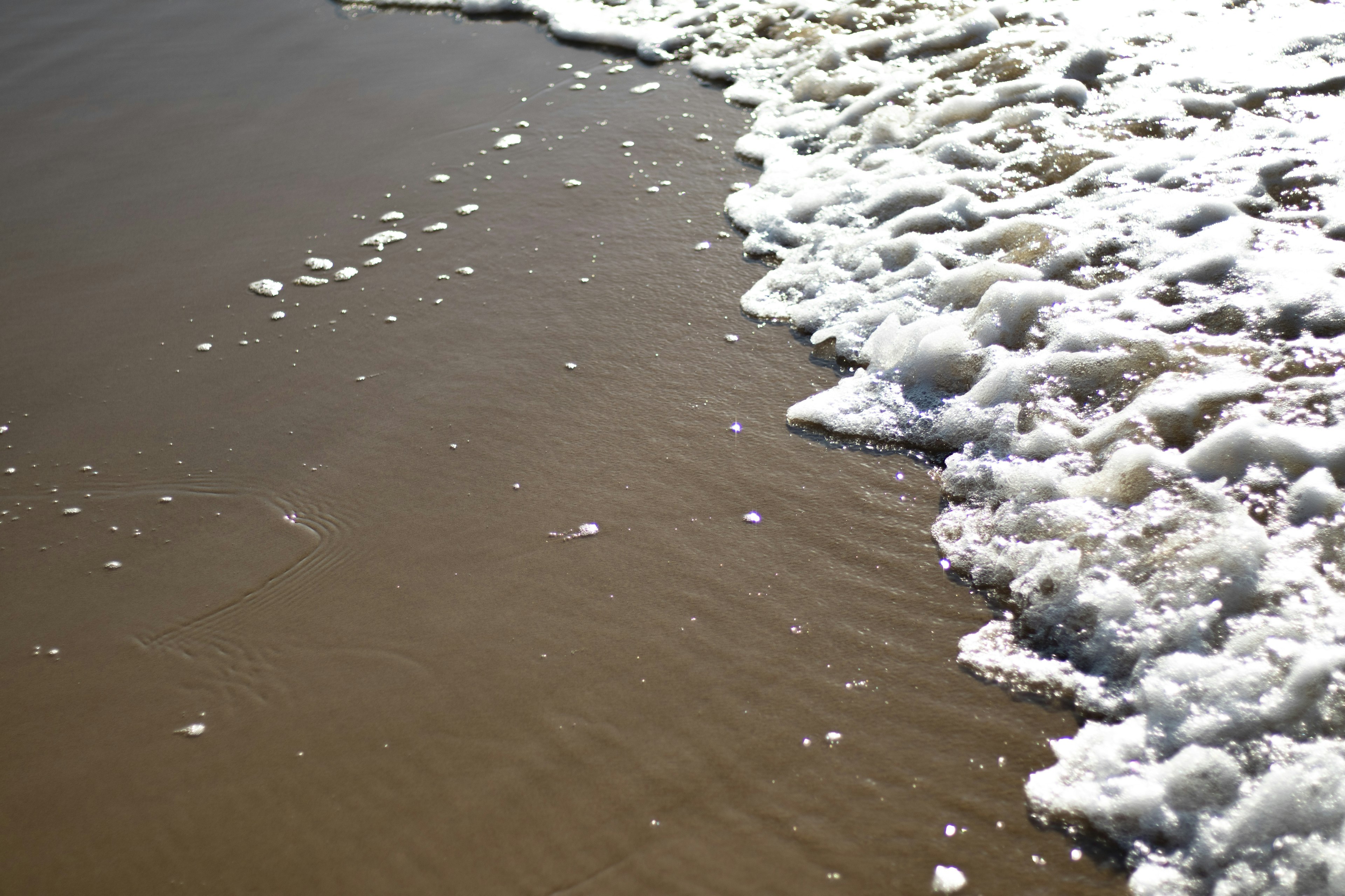 Wellen, die an einen Sandstrand mit weißem Schaum und braunem Sand schlagen