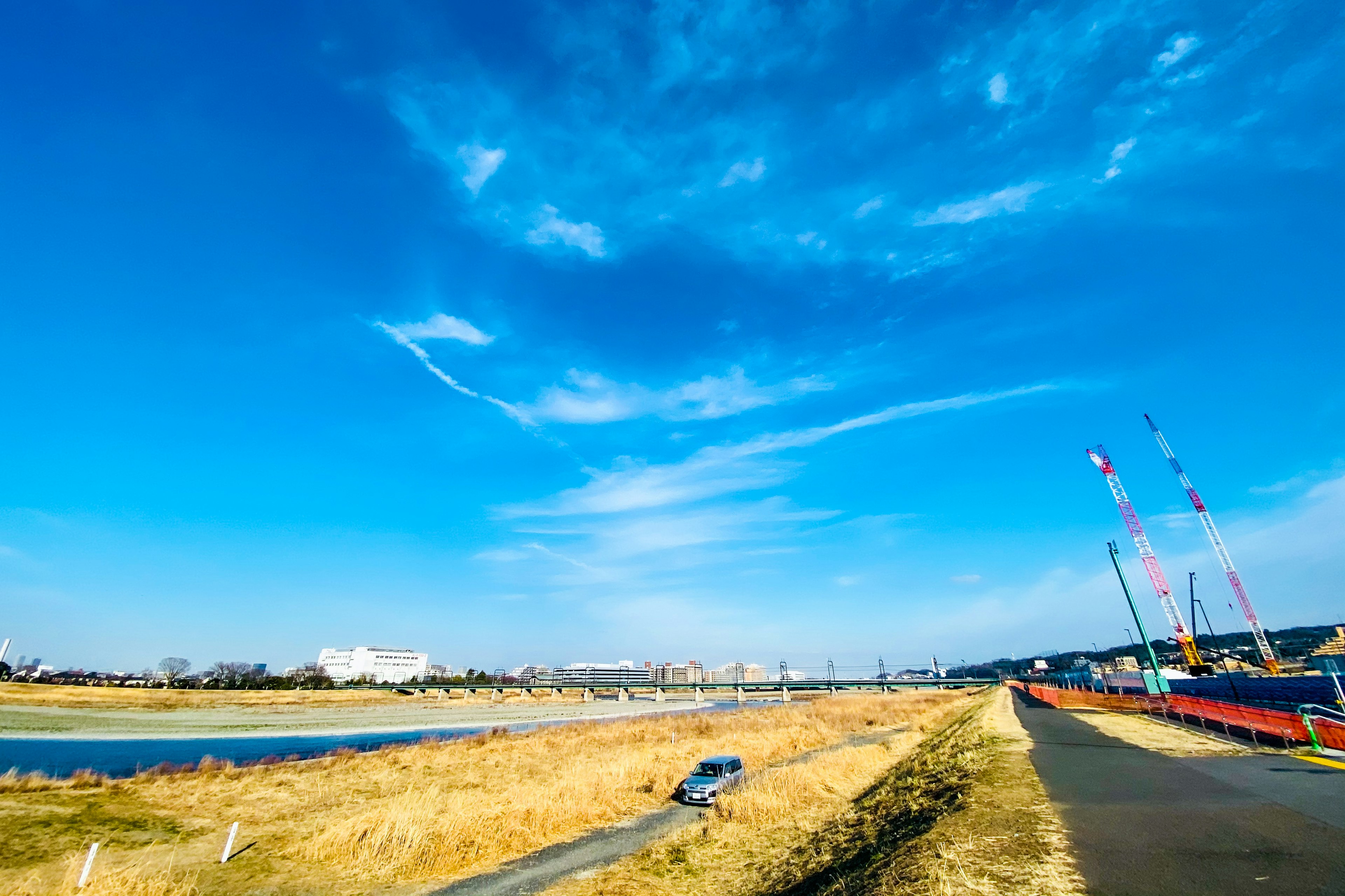 青空の下、川のほとりに広がる草原と道路が見える風景