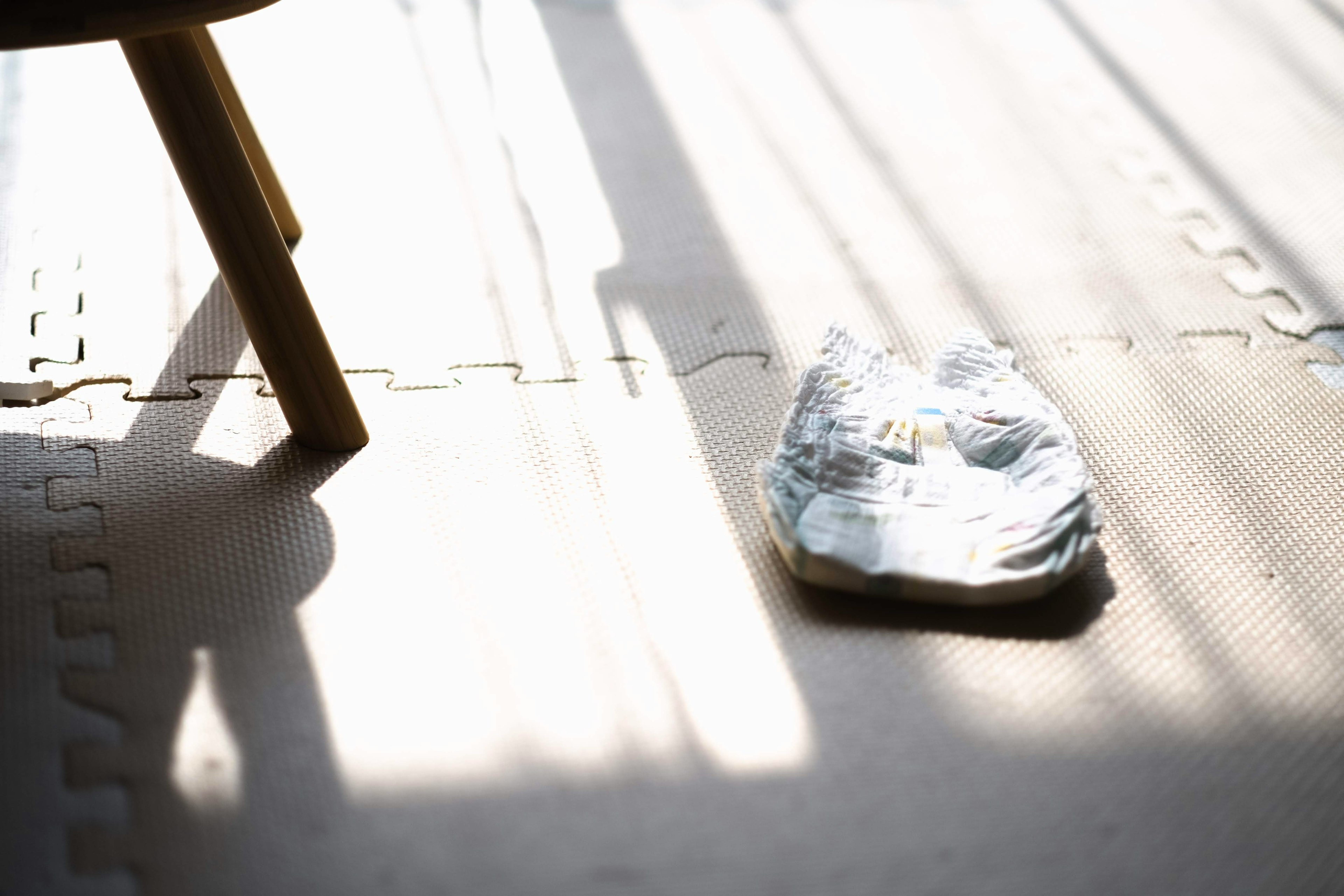 A room with a slipper on the floor and a chair leg in sunlight