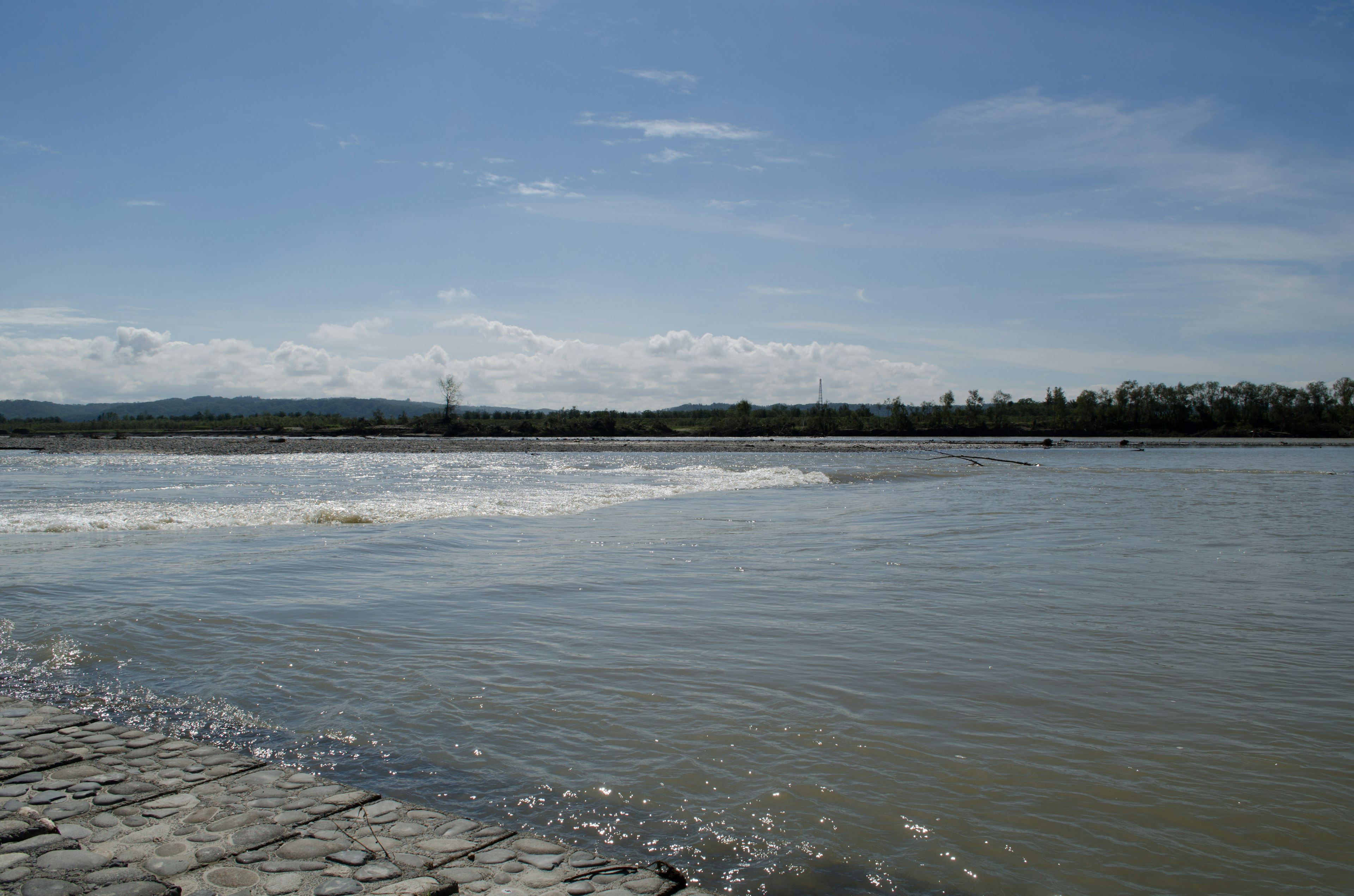 Vista panoramica di un fiume con onde sotto un cielo azzurro molo in pietra visibile