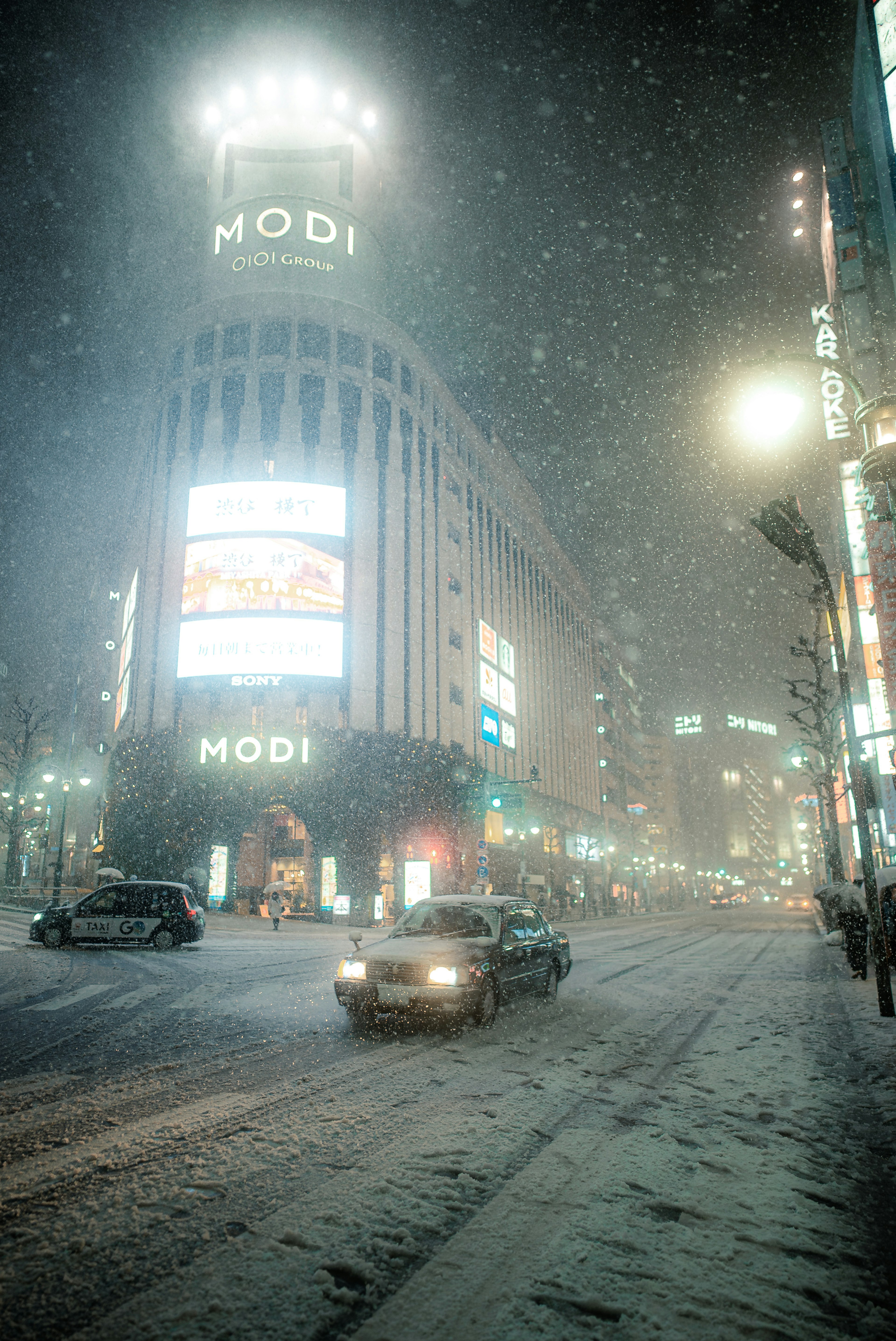 雪が降る夜の都市風景 モディビルと車の通行